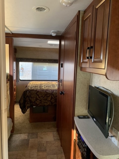 Inside this RV rental: a hallway with tiled floor leads to a carpeted bedroom, featuring wood cabinets, TV, & entertainment.. Forest River Sunseeker 2013