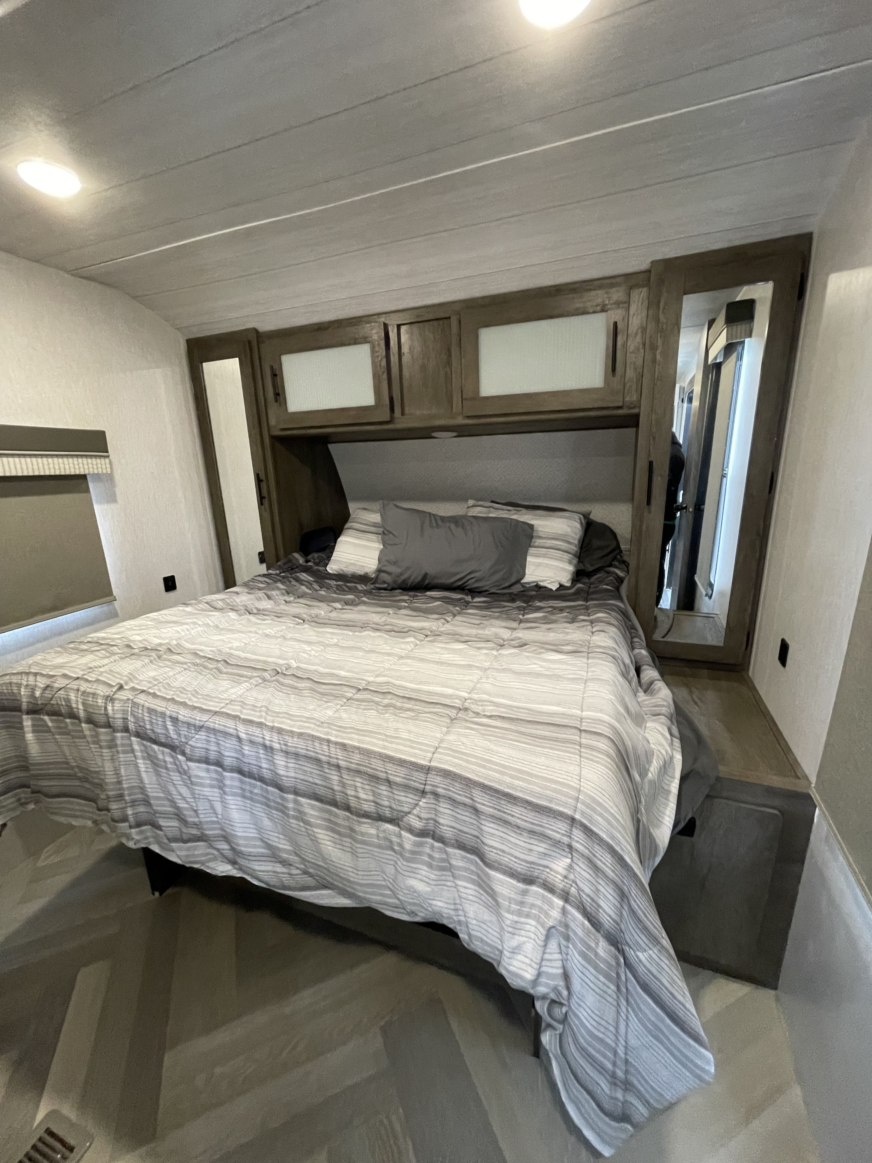 RV rental bedroom with gray and white striped bedding, overhead cabinets, and a full-length mirror, showcasing a compact interior.. Forest River Salem 2022