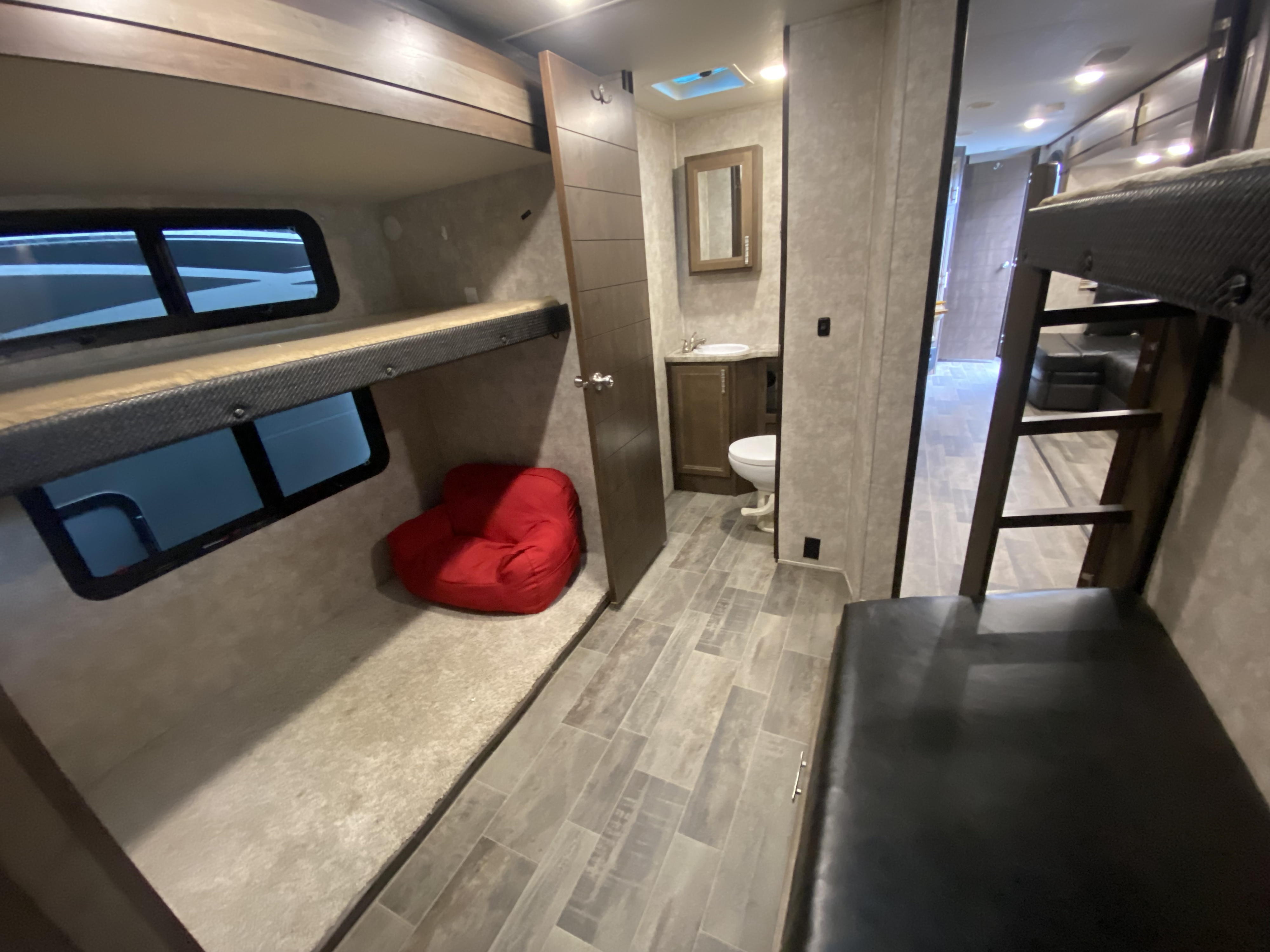 Explore this RV rental's cozy interior, featuring built-in bunk beds with windows, a red bean bag, and a compact bathroom.. Open Range Light 2019