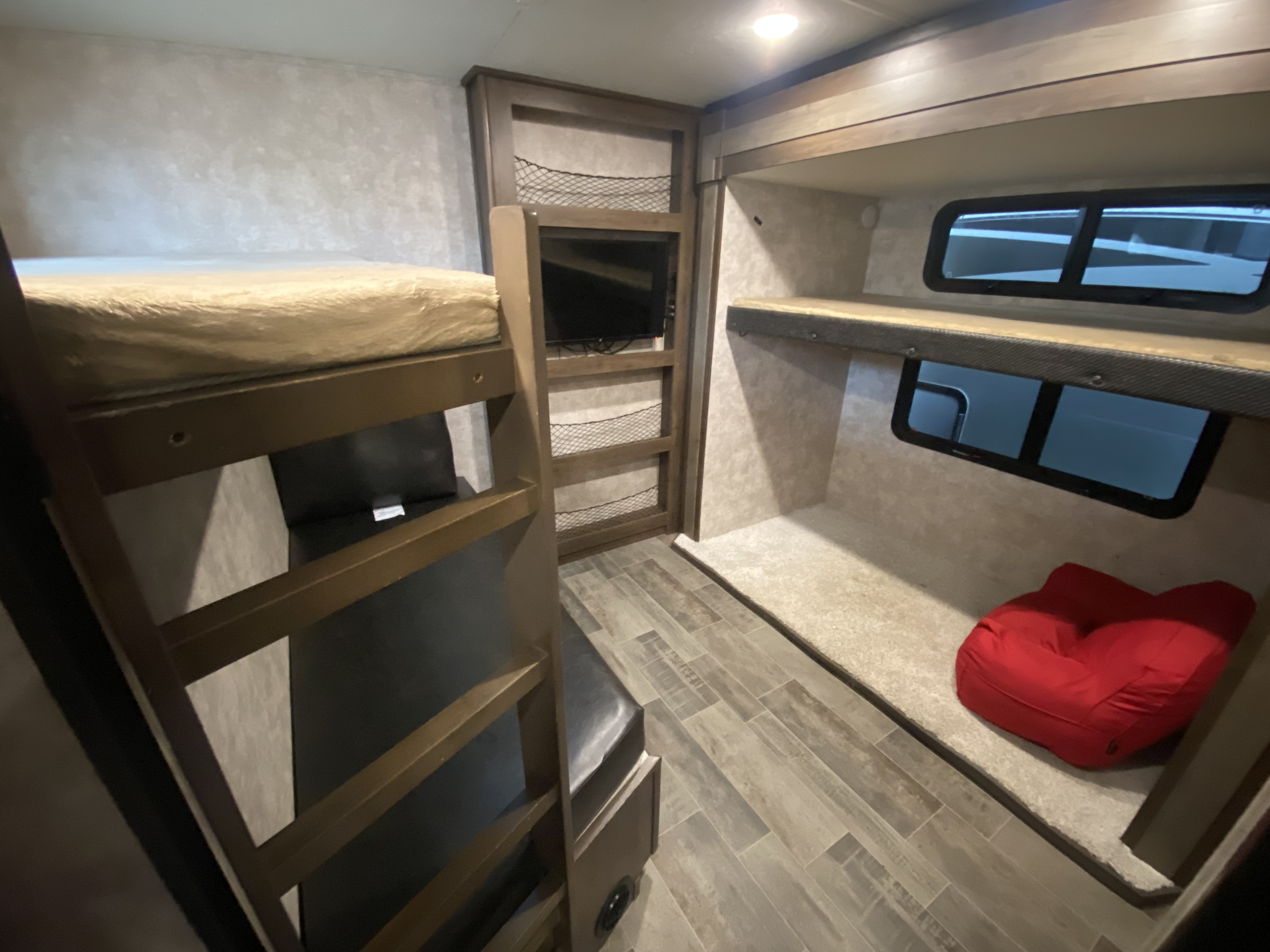 A view of the interior of an RV rental showing stacked bunk beds, a mounted TV, storage nets, and windows for cozy travel.. Open Range Light 2019