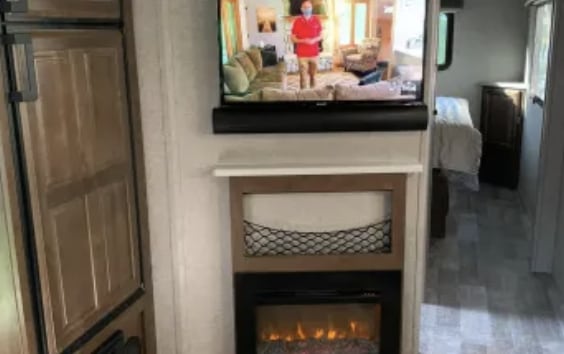 RV rental living space with TV, soundbar, electric fireplace, storage net. Kitchen unit left, bedroom hallway right.. Forest River Rockwood Mini Lite 2019