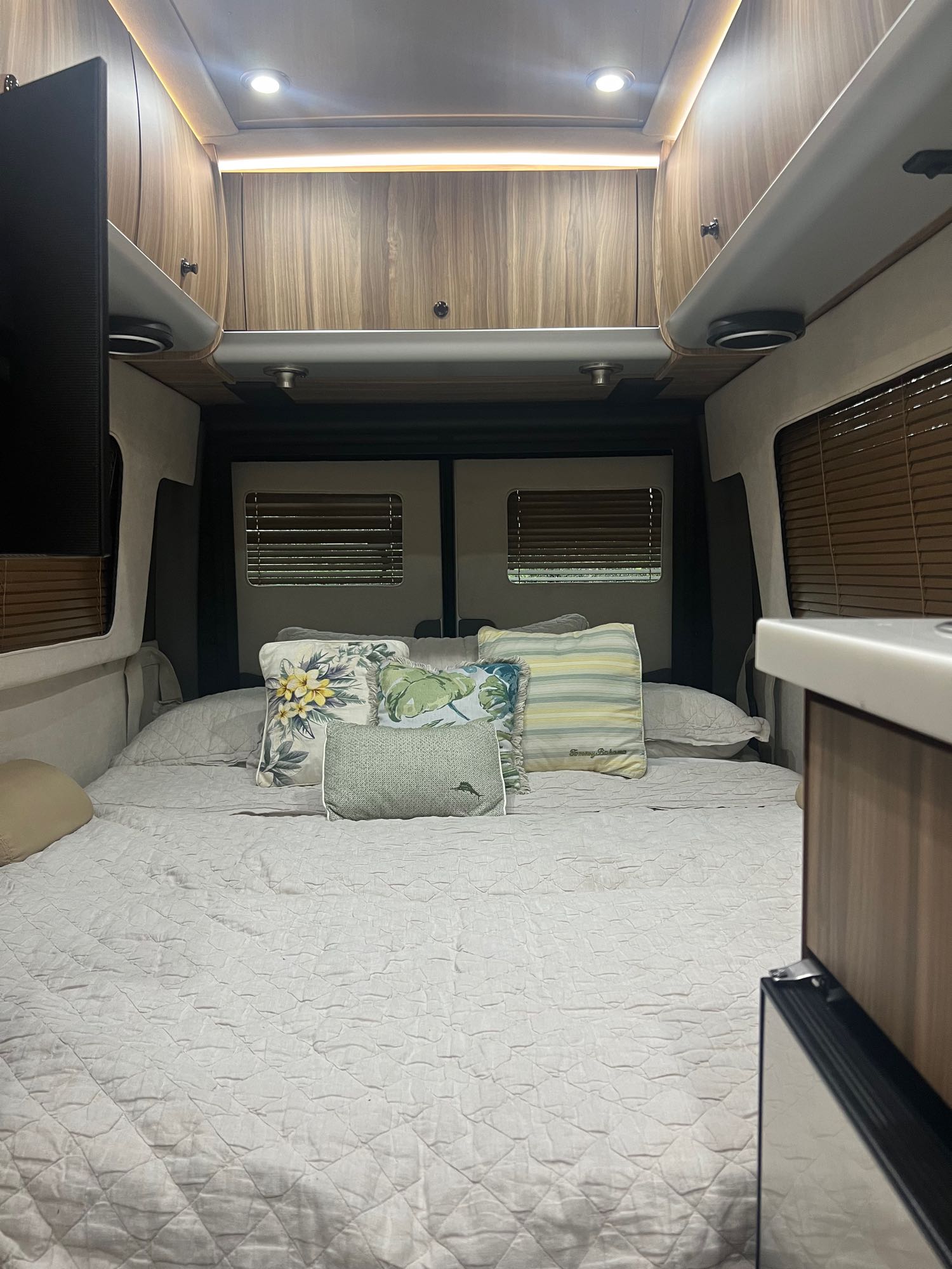 Comfortable RV rental interior featuring a large bed with decorative pillows, wood paneling, and bright overhead lights.. Airstream Interstate 2018