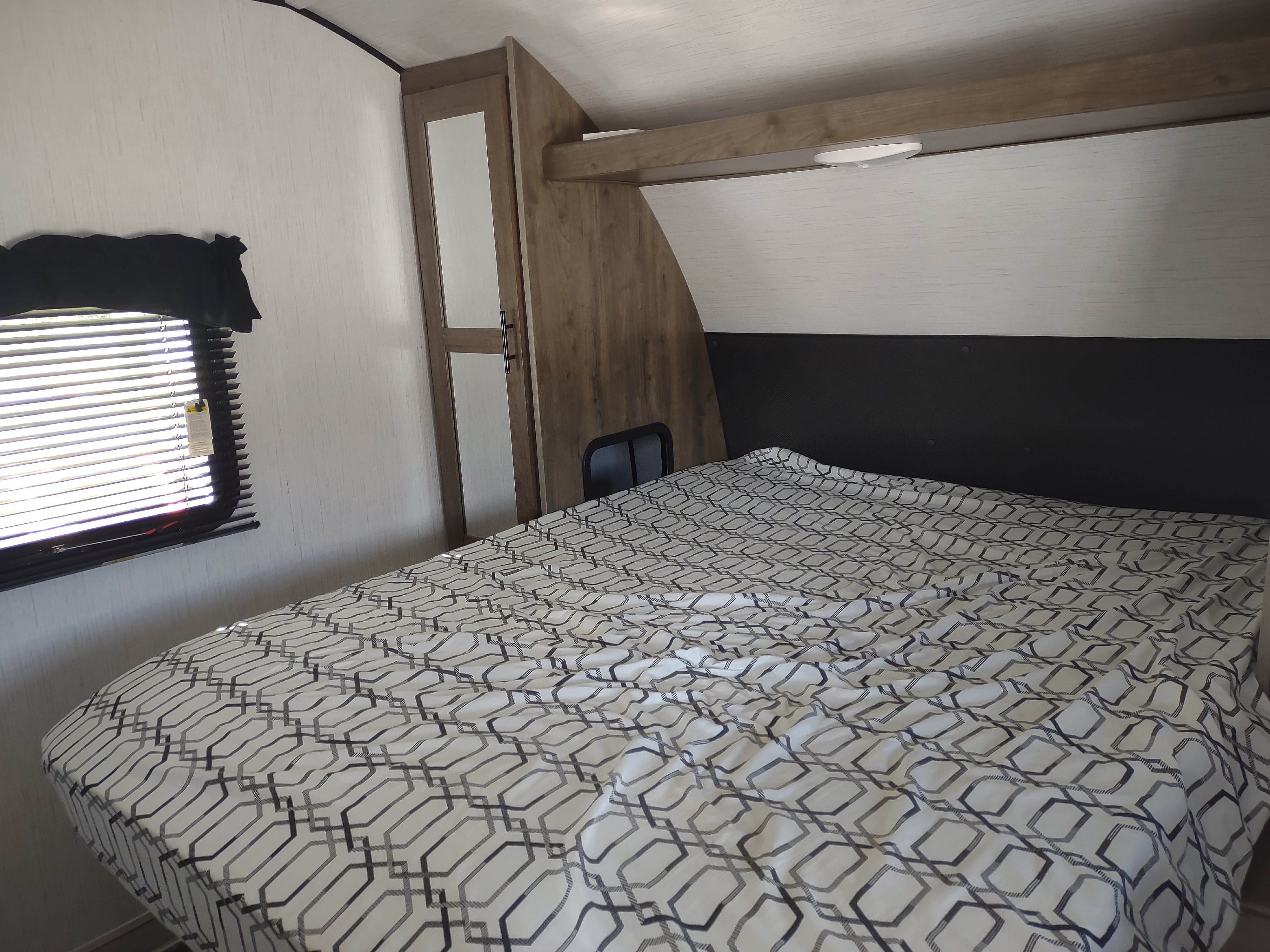Cozy RV rental bedroom with a patterned comforter, window blinds, and wood-toned storage.. Heartland RVs Pioneer 2021