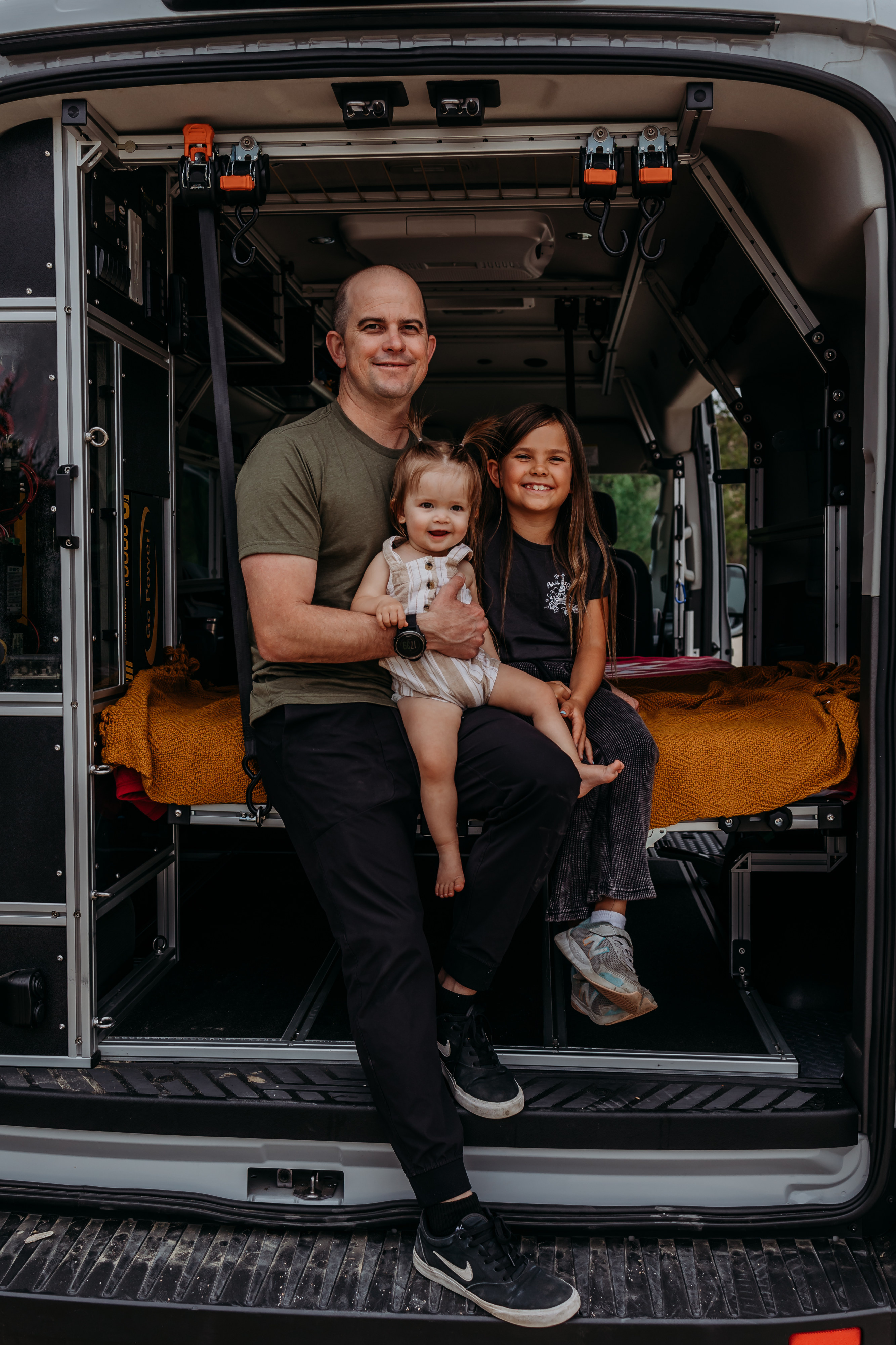 Smiling family inside a custom RV rental. A dad holds a toddler, an older child sits beside them in the camper van.. Ford Vandoit 2022