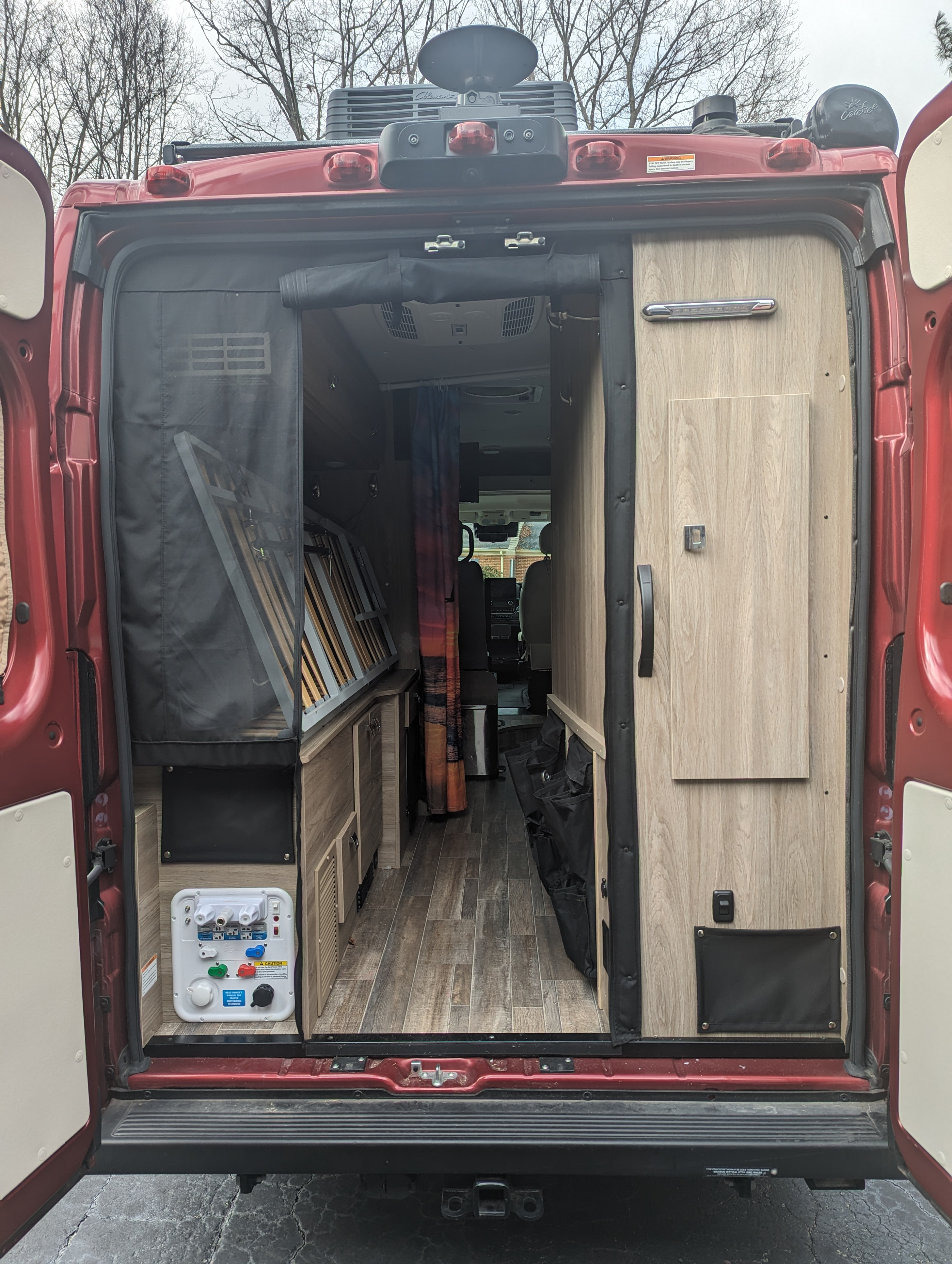 Camper van RV rental: Rear interior view of a red van with open doors, showing kitchen, fold-up bed, & storage.. Winnebago Travato 2023