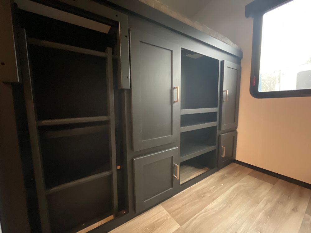 RV rental interior: Dark storage cabinets, entertainment center, and a bunk/storage system with ladder access. Functional design.. Keystone RV Outback 2023
