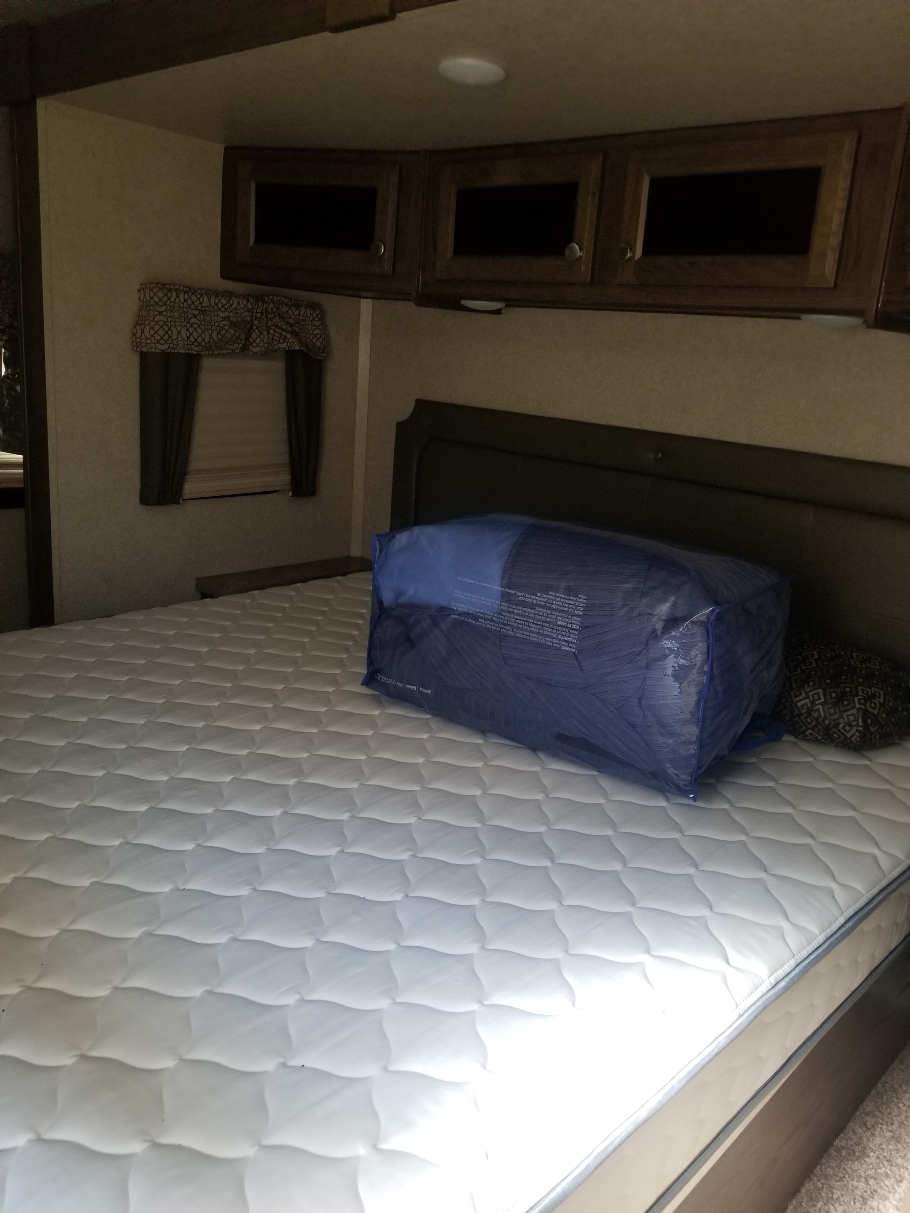 This RV rental bedroom features a fresh mattress, ready with a bedding bag. Overhead cabinets and a window complete the cozy travel space.. Forest River Flagstaff Classic Super Lite 2018