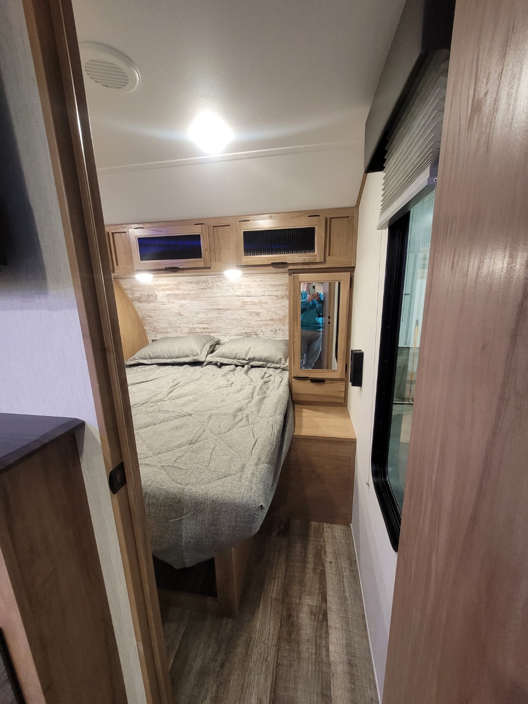 Step inside this modern RV rental bedroom, featuring a neatly made bed, wooden cabinetry, and bright lighting.. Forest River 26 DBH 2024