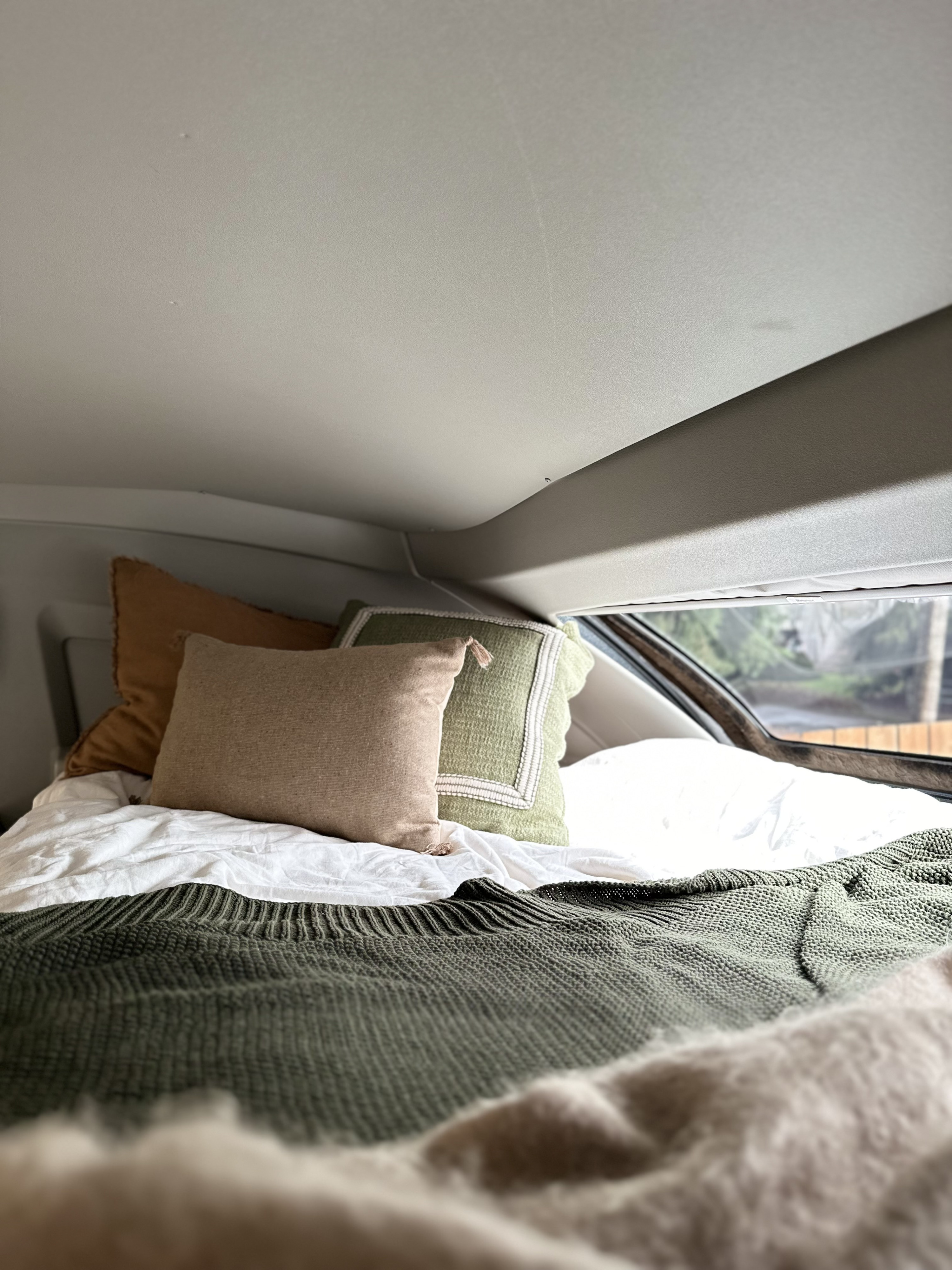 This RV rental offers a cozy bed: white sheets, green knit blanket, and comfy pillows visible inside a vehicle.. Coachmen Prism Select 2023