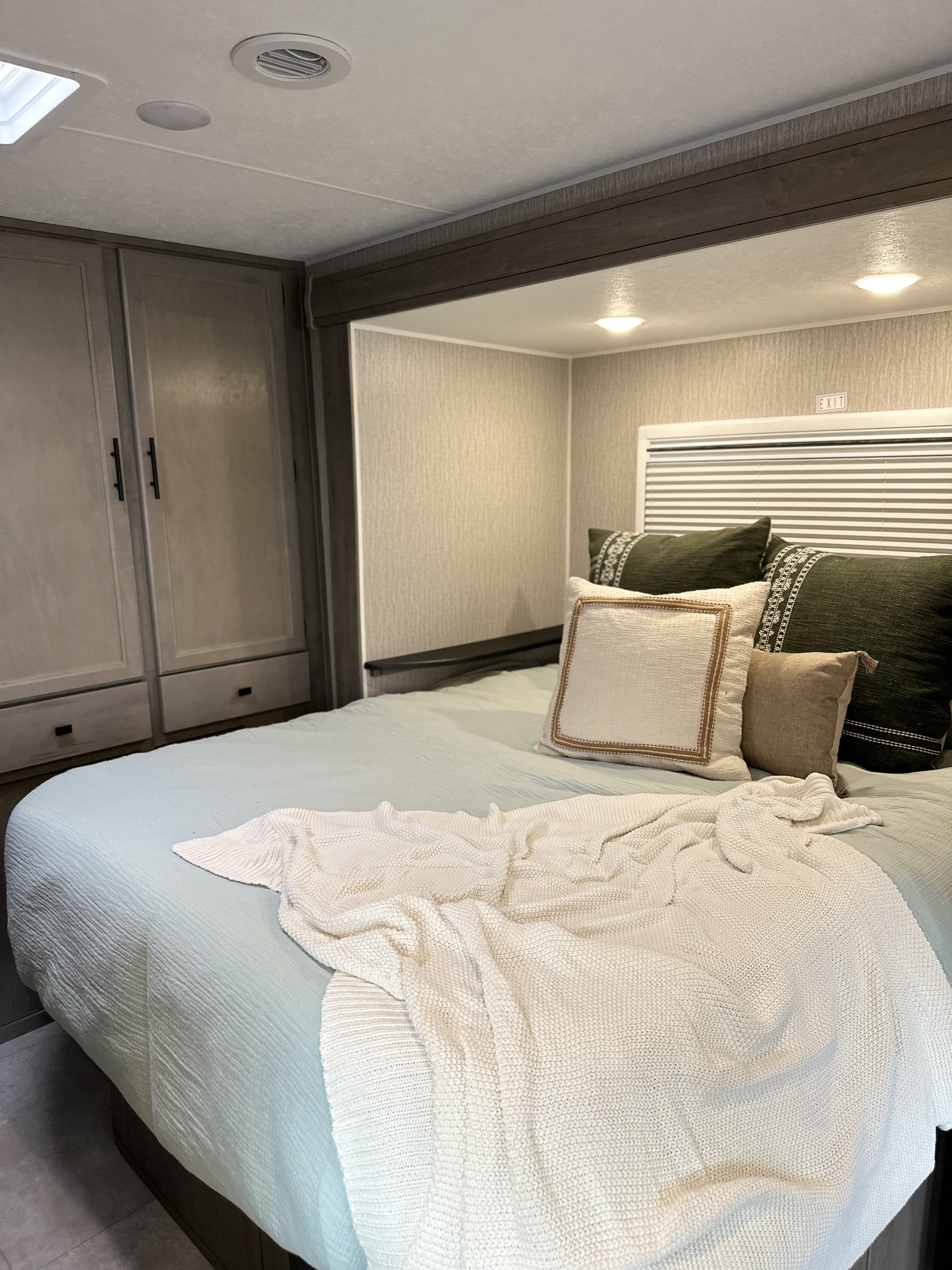 Relaxing RV rental bedroom: light blue bed with a white throw, cozy pillows, and built-in storage cabinets.. Coachmen Prism Select 2023