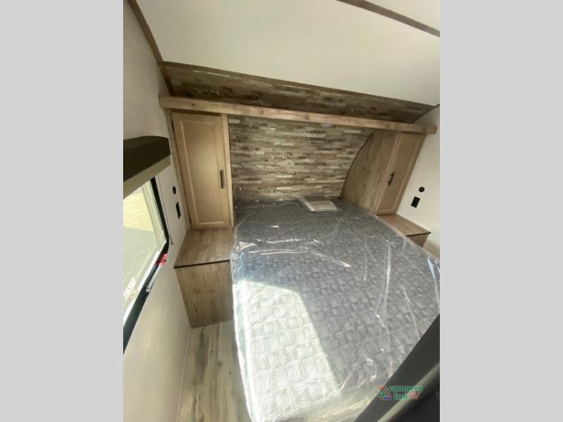Inside an RV rental: a compact bedroom features a bed with plastic covering, wood-paneled headboard, and storage.. Gulf Stream Friendship 268BH 2024
