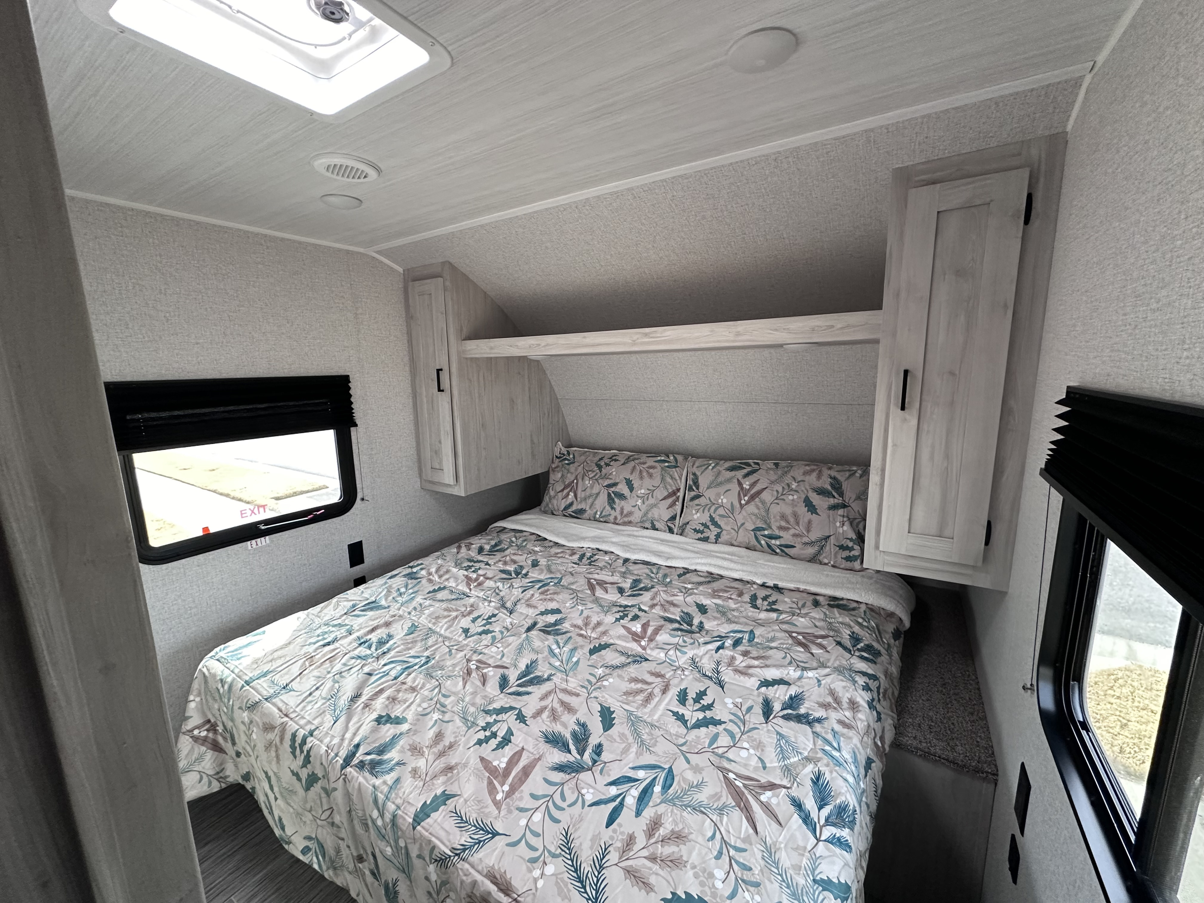 Compact RV rental bedroom featuring a comfy bed with nature-themed bedding, overhead storage, and windows.. East to West Silver Lake 2023