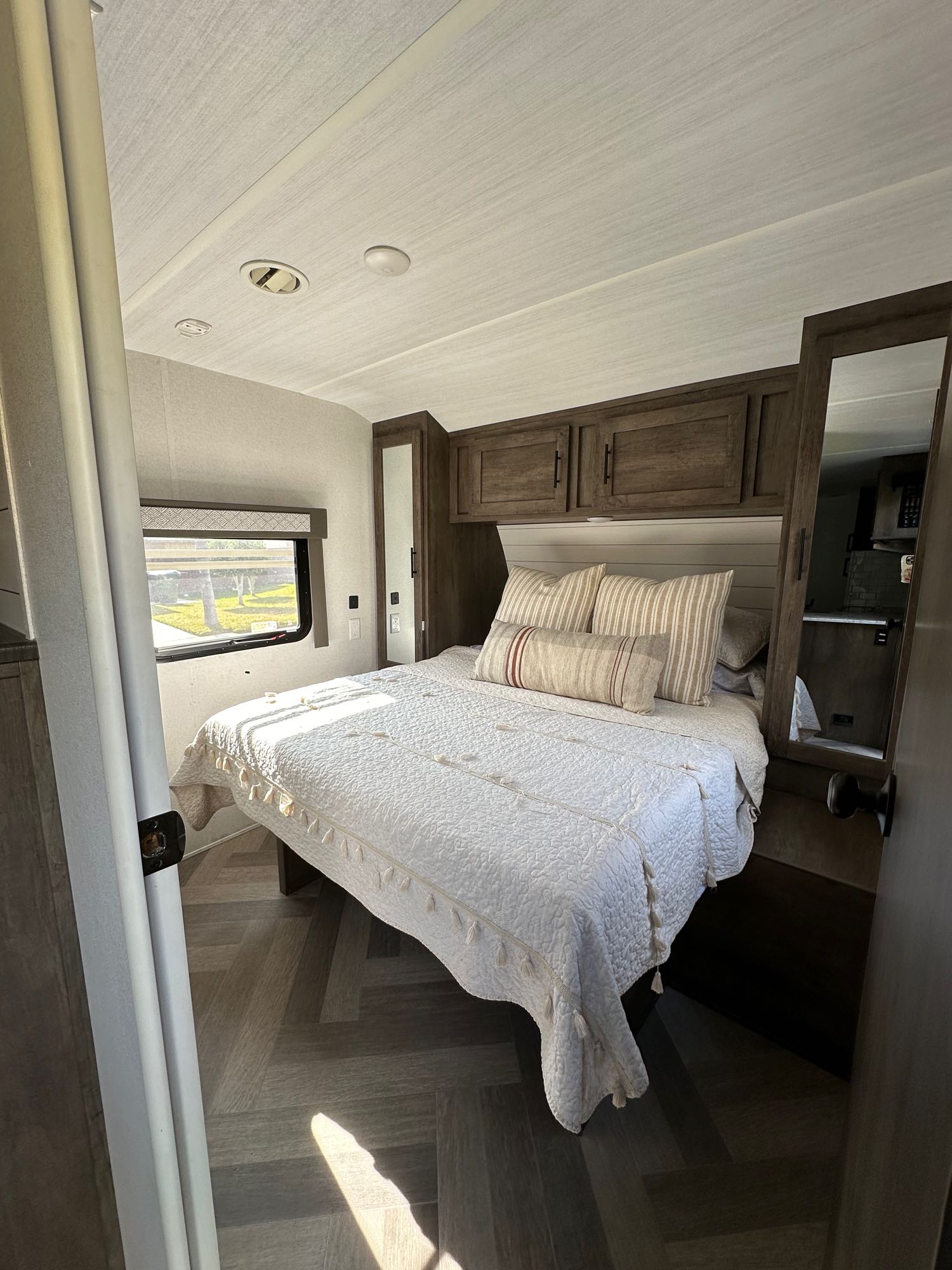 This inviting RV rental bedroom features a comfy bed, overhead cabinets, and a mirrored wardrobe reflecting the kitchen beyond.. Forest River Salem 2021