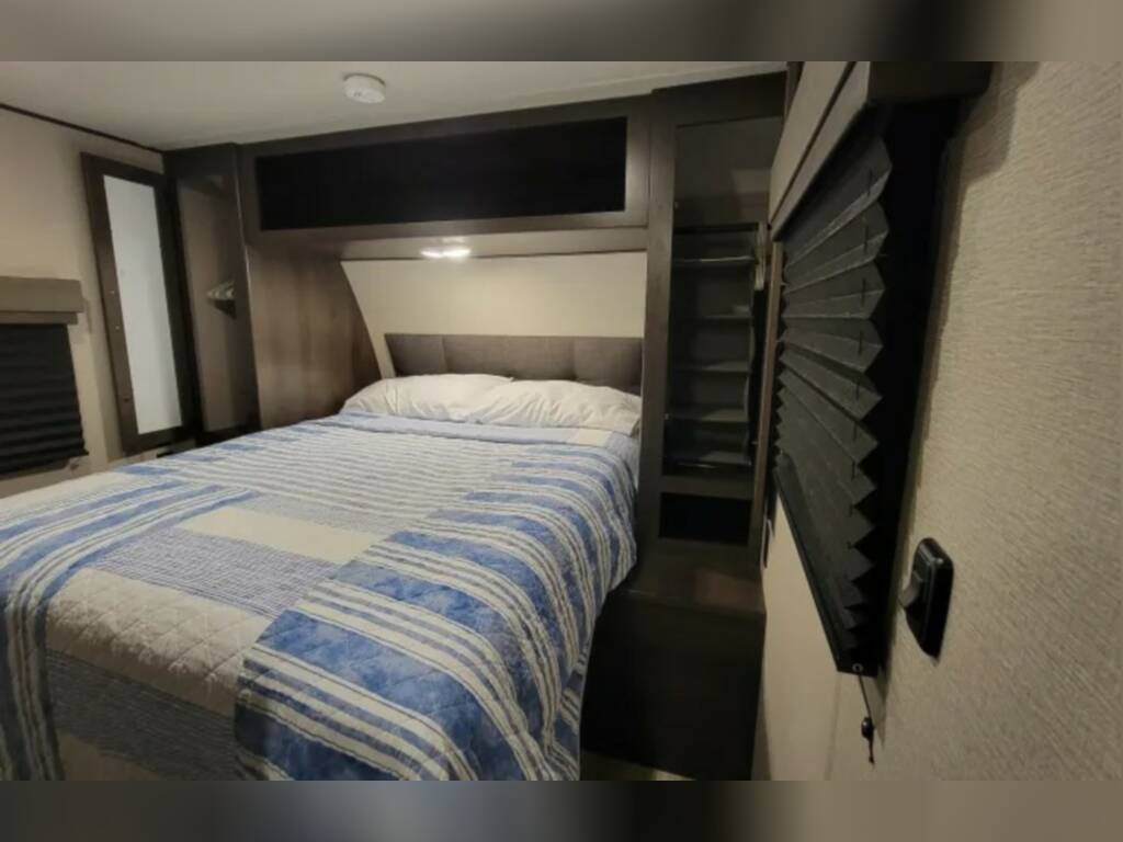 Cozy RV rental bedroom with a blue & white bed, built-in storage, and accordion blinds for privacy.. Grand Design Other 2022