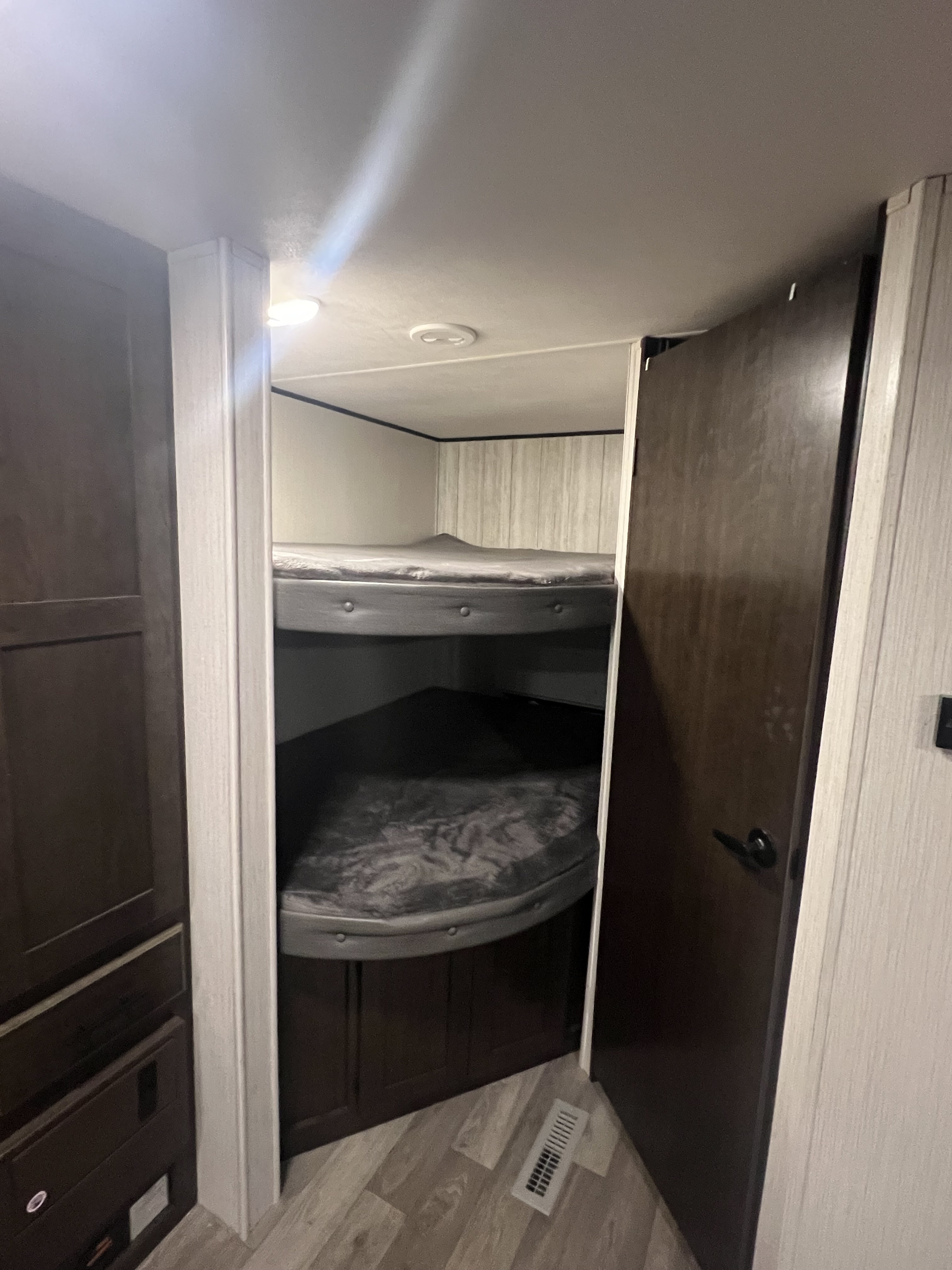 Compact RV rental interior: two cozy bunk beds with grey mattresses, dark wood storage, and bright lighting.. Heartland RVs Pioneer 2020