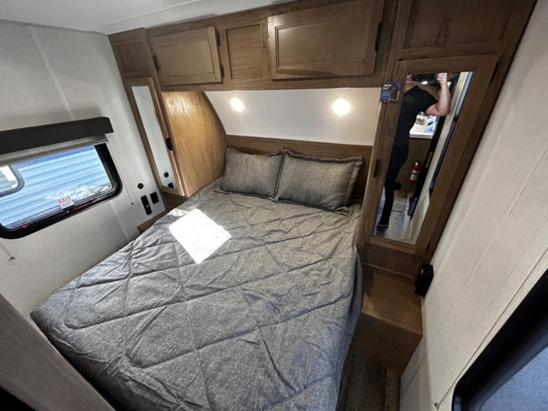 RV rental bedroom: compact, featuring a gray bed, wood cabinetry, a mirrored wardrobe, and an exit window.. Forest River Cherokee Grey Wolf 23DBH 2024