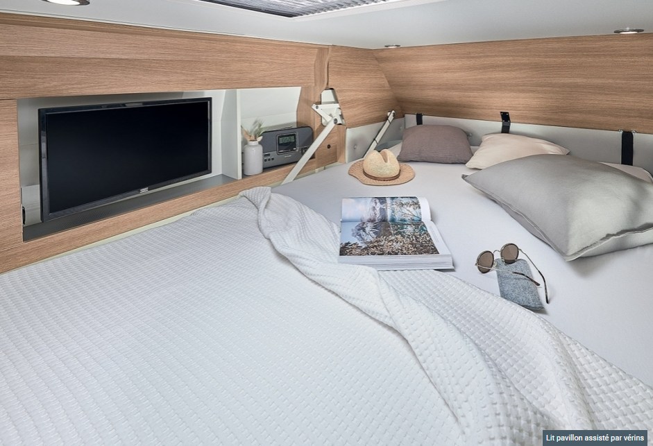 Relax in this modern RV rental bedroom featuring a comfy bed, integrated TV, and warm wood finishes.. CAMPEREVE FAMILY VAN 2022