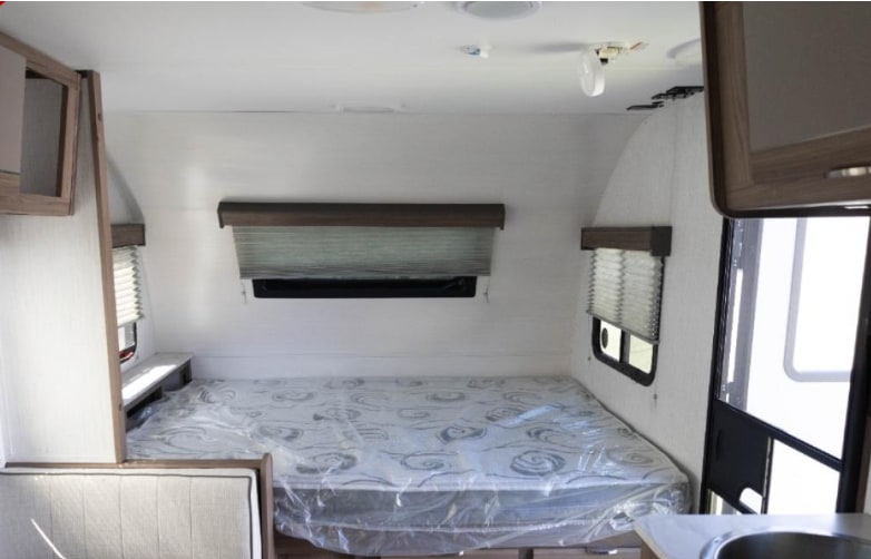 View of an RV rental bedroom with a plastic-covered mattress, windows with blinds, and built-in cabinets.. Cruiser RV Hitch 2024