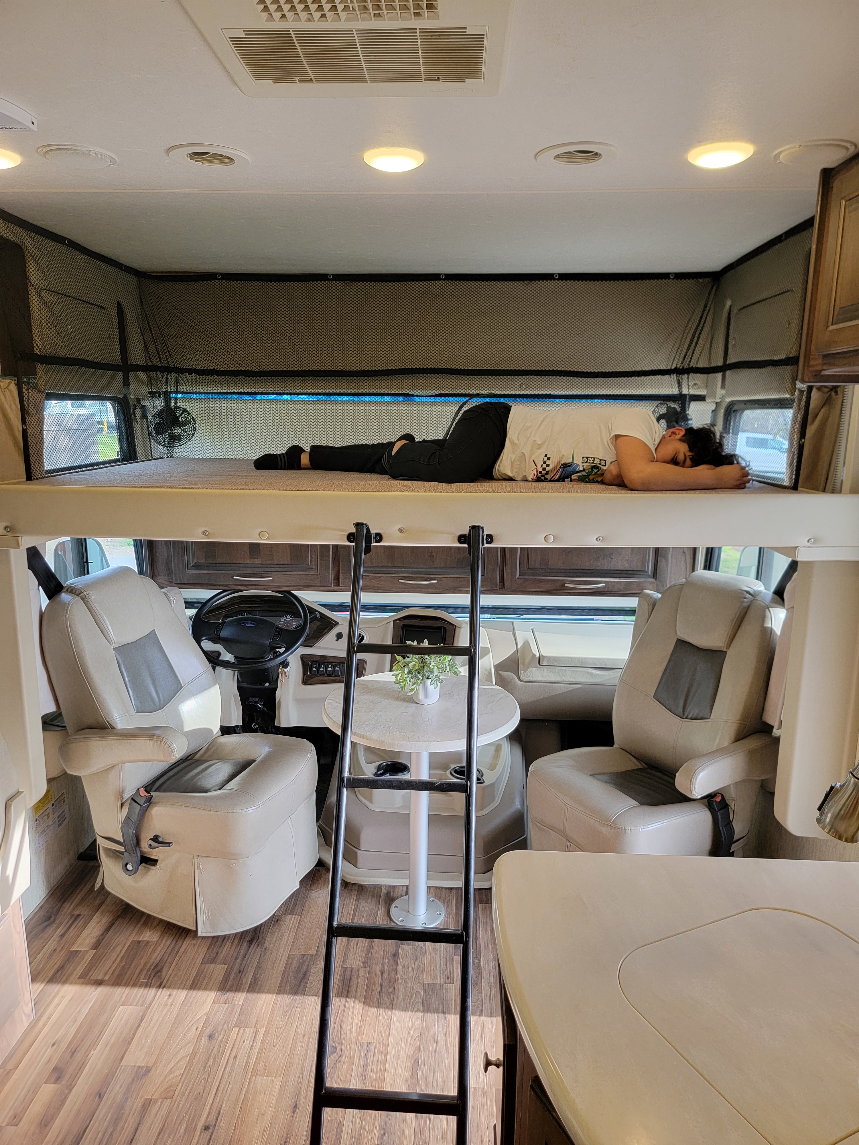 Cozy RV rental interior: A person naps in the overhead bunk, showing comfortable travel space.. Coachmen Mirada 2018