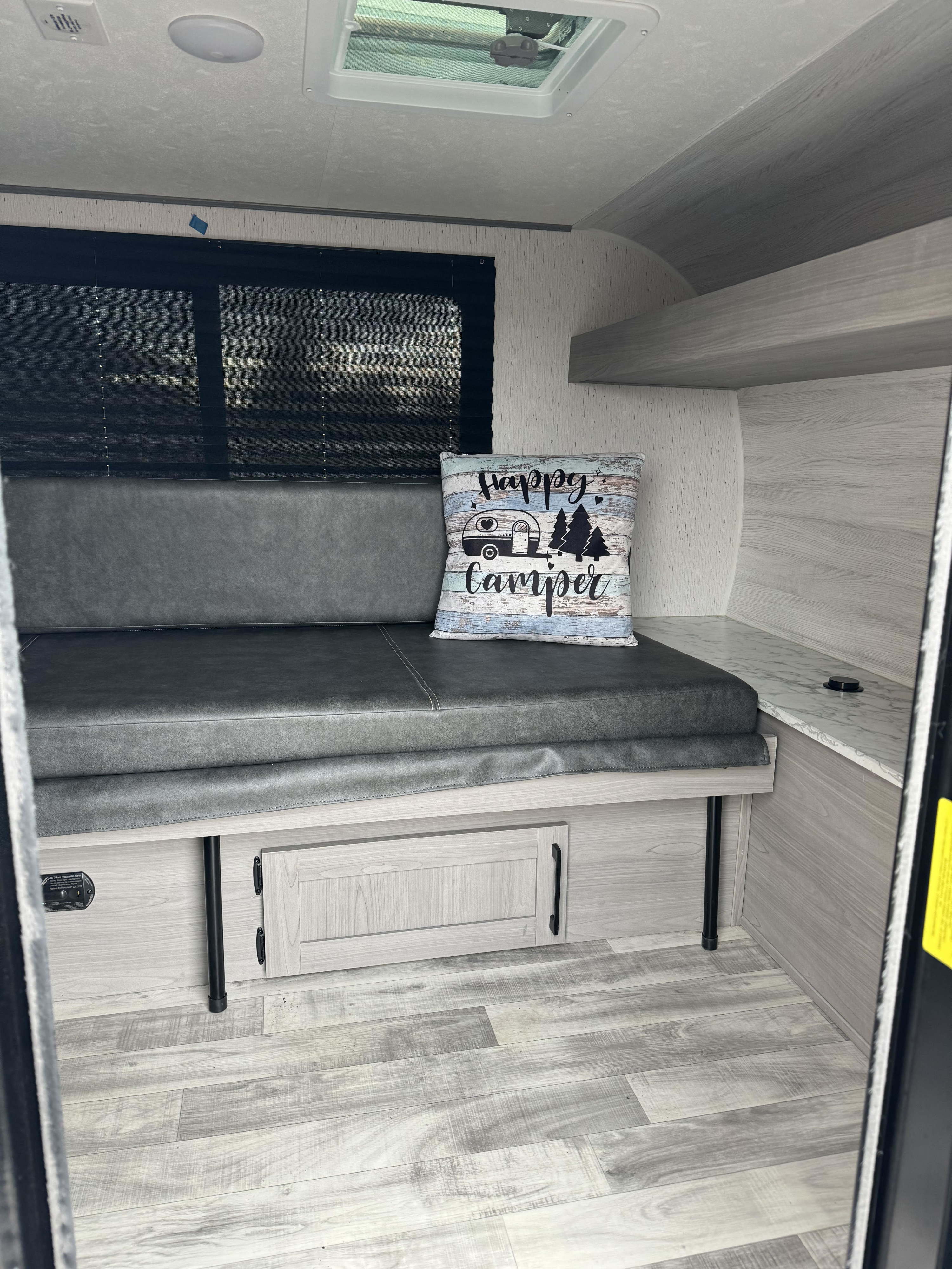 Modern RV rental interior with comfortable grey bench seating, light wood-grain details, ample storage, and a large window.. Coleman Rubicon 2023