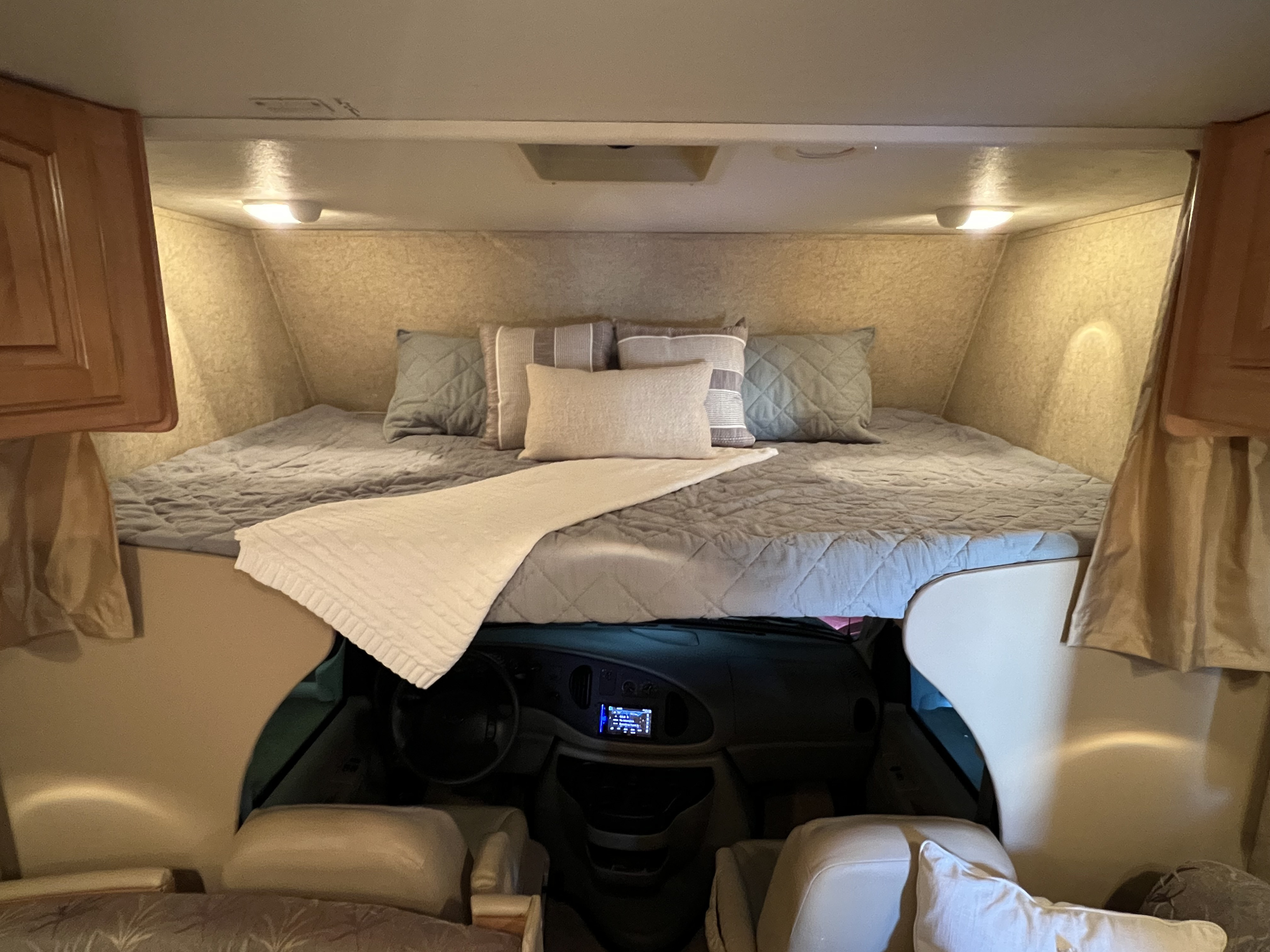Cozy RV rental cab-over bunk bed with comfortable bedding, offering a view into the driver's cockpit below.. Jayco Greyhawk Sport 2008