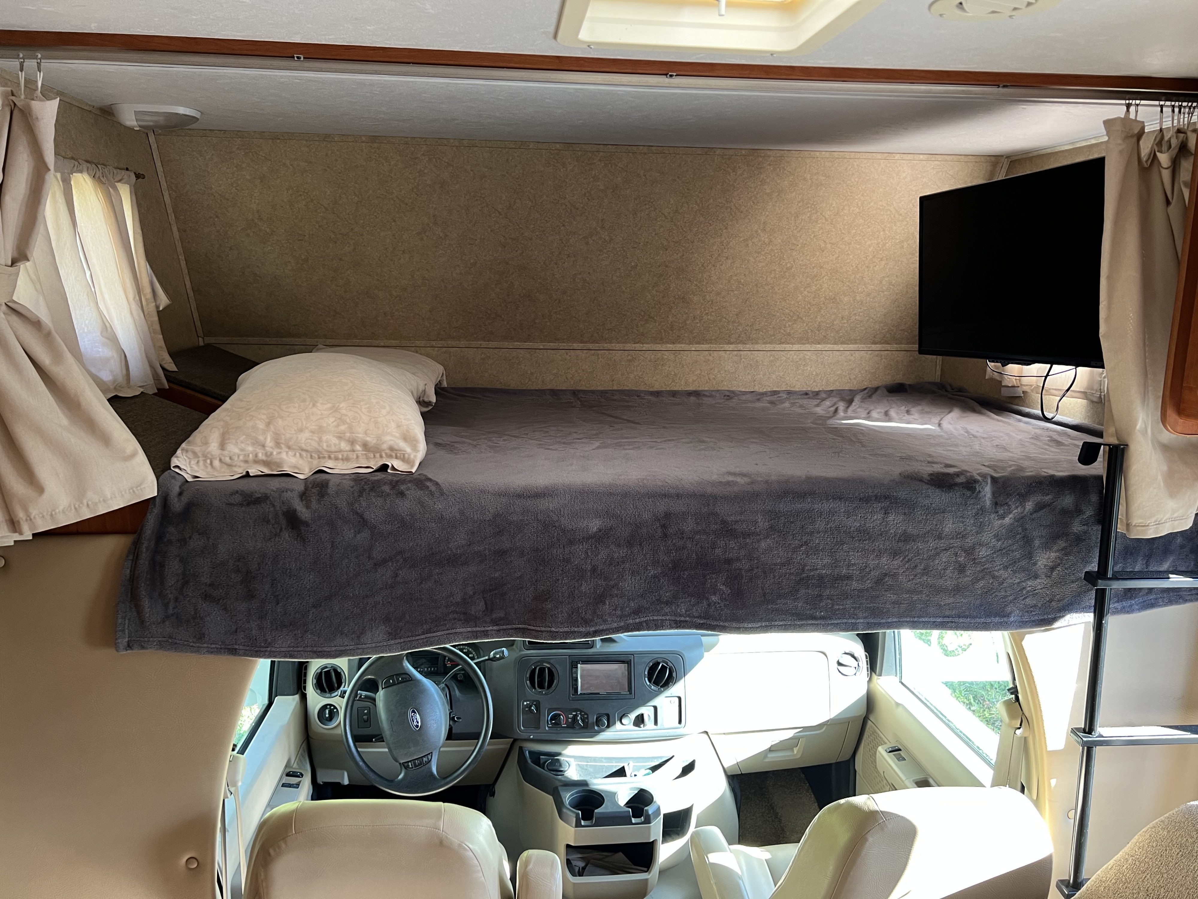 Cozy RV rental cab-over bunk with TV, overlooking the driver's cockpit.. Forest River Sunseeker 2010