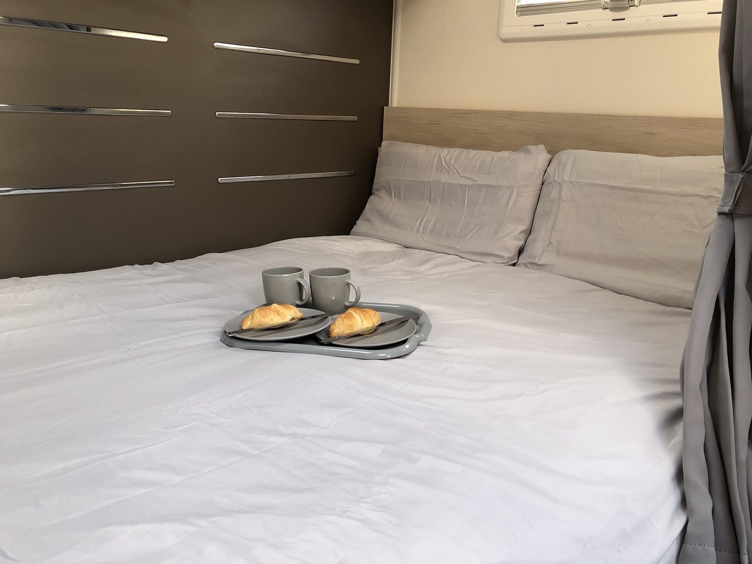 A cozy RV rental bedroom: comfortable bed with croissants & coffee on a tray, ready for breakfast.. Chausson 514 2019