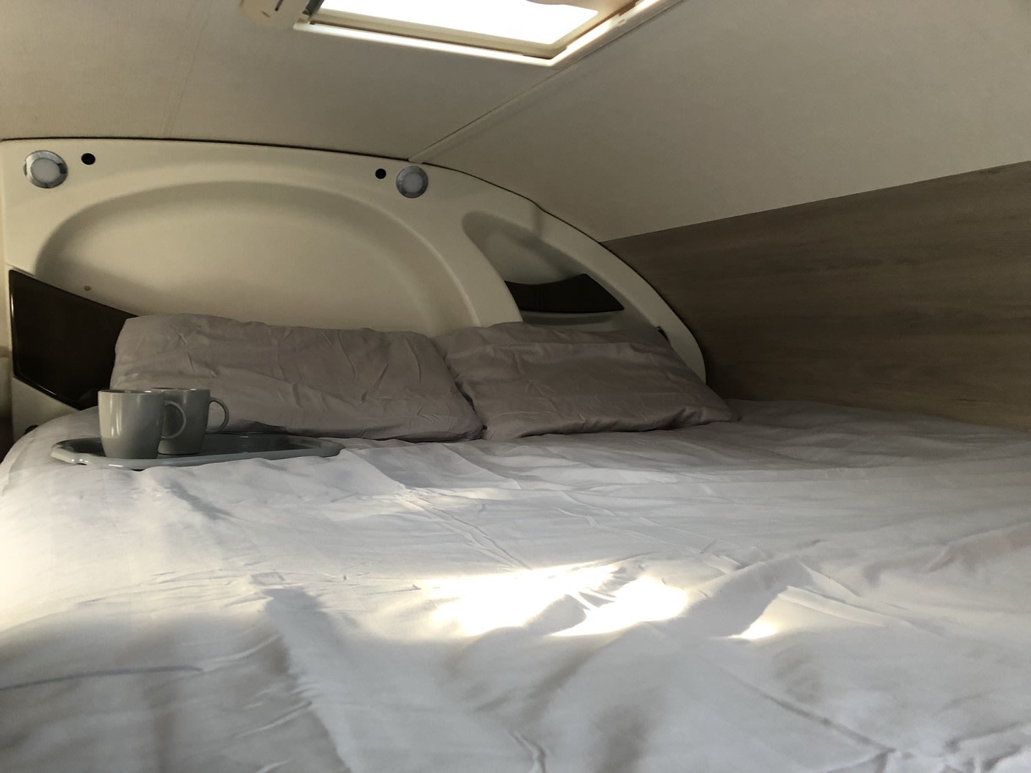 Relaxing RV rental interior: a comfy bed with pillows, mugs on a tray, and sunlight from the skylight.. Chausson C646 2019