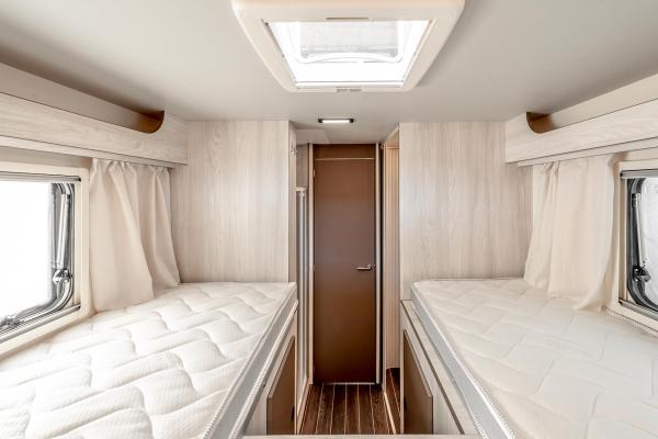 An RV rental bedroom featuring twin bunk beds with white mattresses, light wood paneling, and a central door.. Rimor Kilig 695 2024
