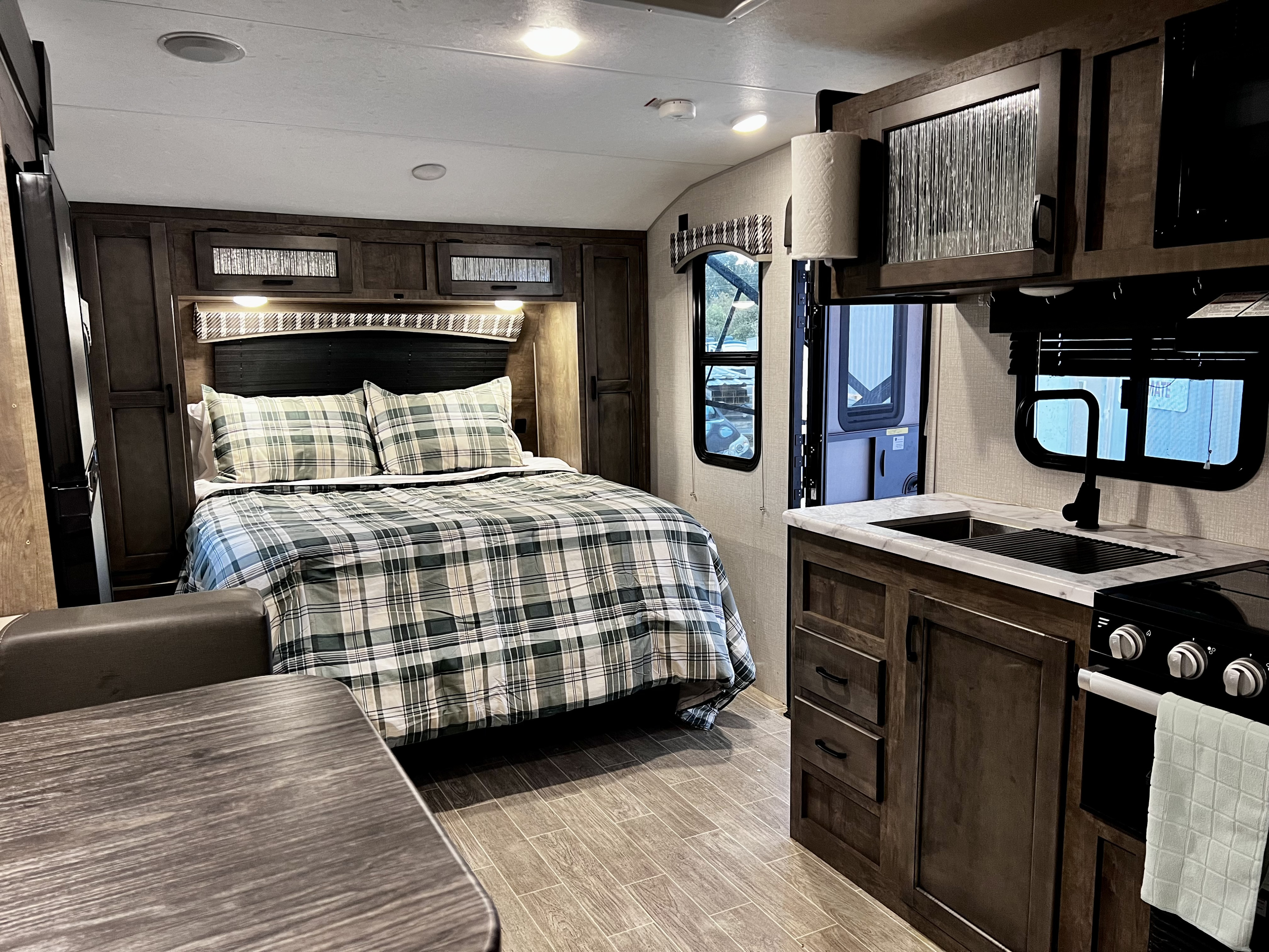 Step inside this cozy RV rental, featuring a comfortable bedroom with plaid bedding and a compact kitchen complete with sink and stove.. Venture Rv Sonic 2022