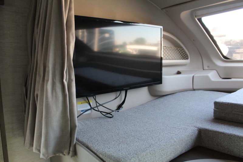 Compact RV rental interior featuring a mounted TV, soft gray bed/seating, curtain, and window. Ideal for travel.. Entegra Coach Esteem 2022