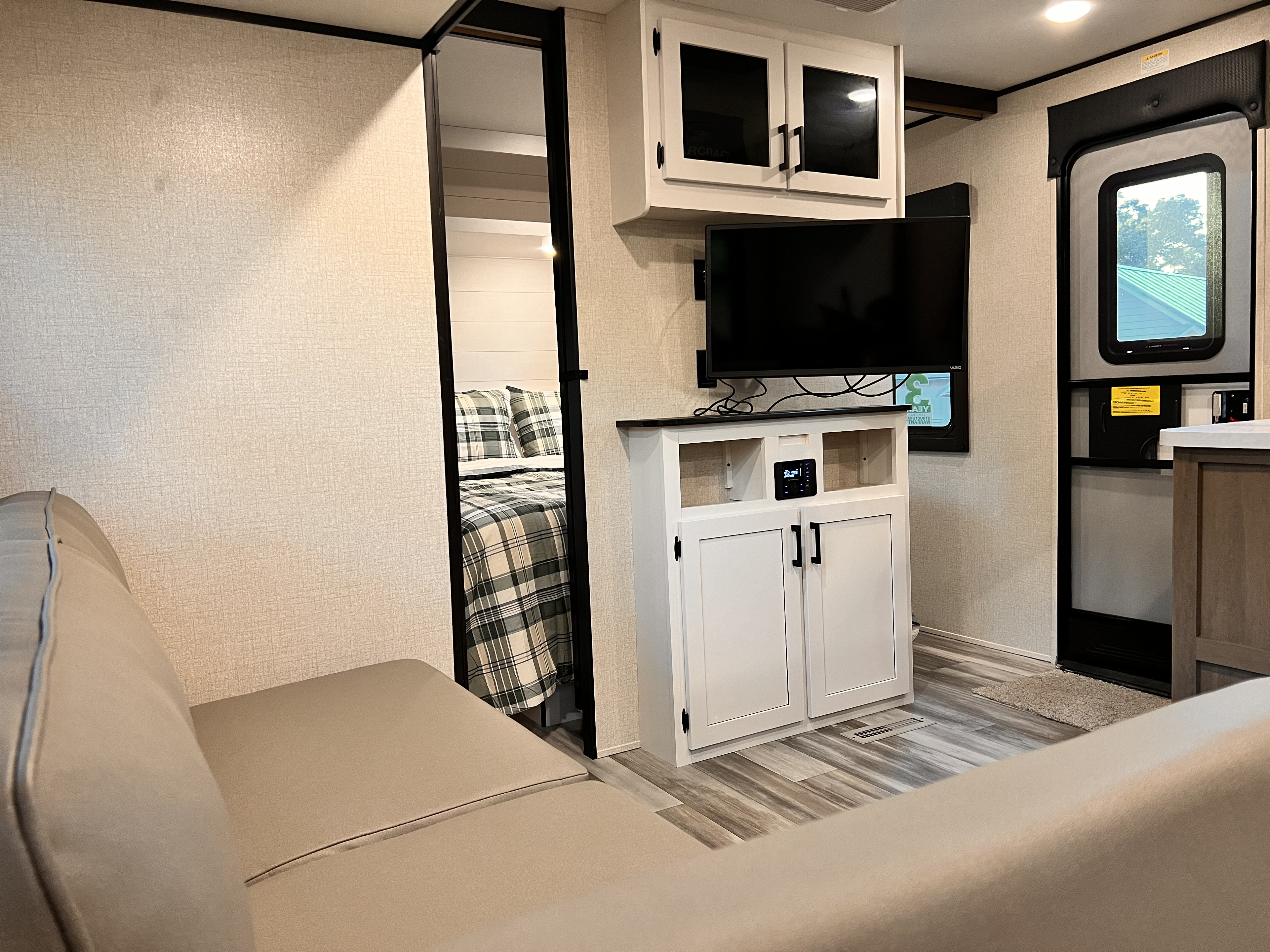 RV rental interior: sofa, entertainment center with TV, open doorway to bedroom with plaid bedding, and exterior door.. Starcraft Autumn Ridge 2024