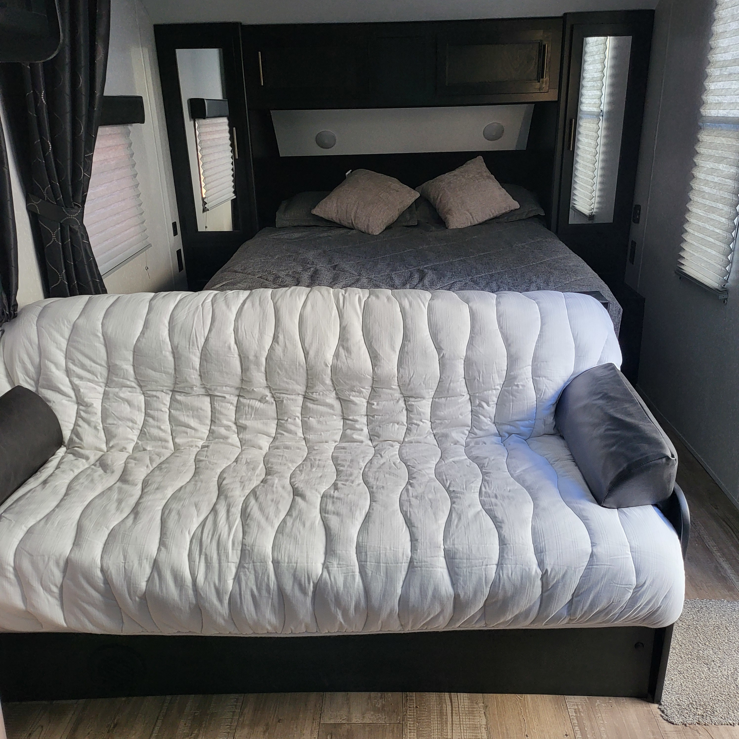 This RV rental features a comfortable bed nestled within dark cabinetry, and a white quilted sofa for a versatile living space.. Forest River Cherokee Grey Wolf 2022