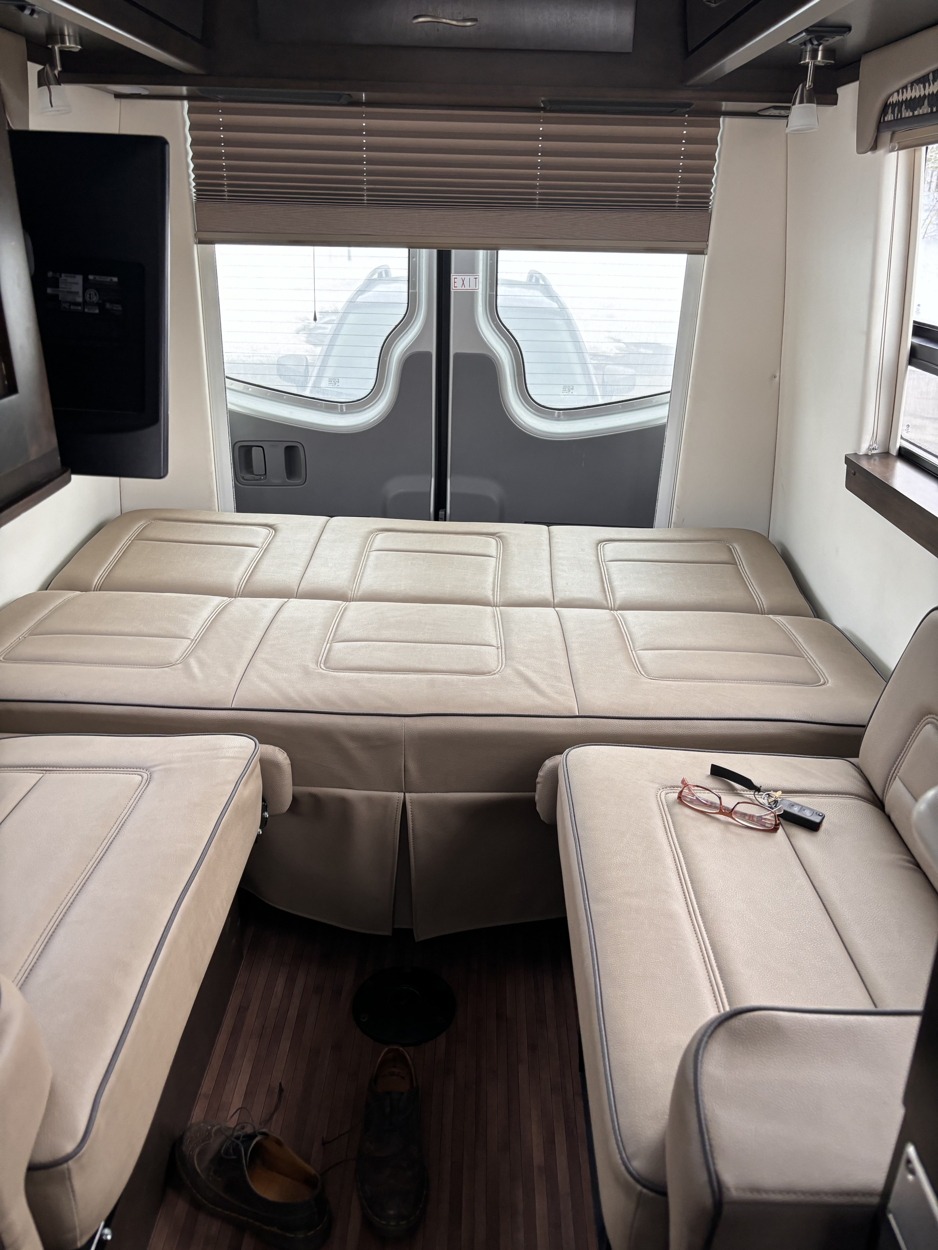 Interior of an RV rental: a light brown leather modular bed, two armchairs, a TV, and rear windows, perfect for trips.. Mercedes-Benz Sprinter RV Motorhome Campervan 2017