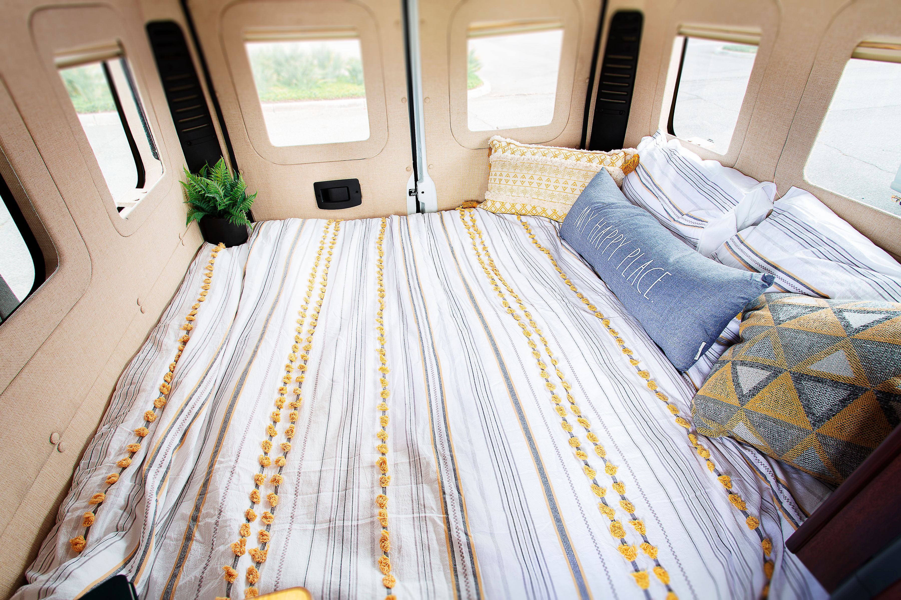 Cozy RV rental interior: A comfortable camper van bed with striped bedding, decorative pillows, and a plant.. Dodge Promaster 2500 2014