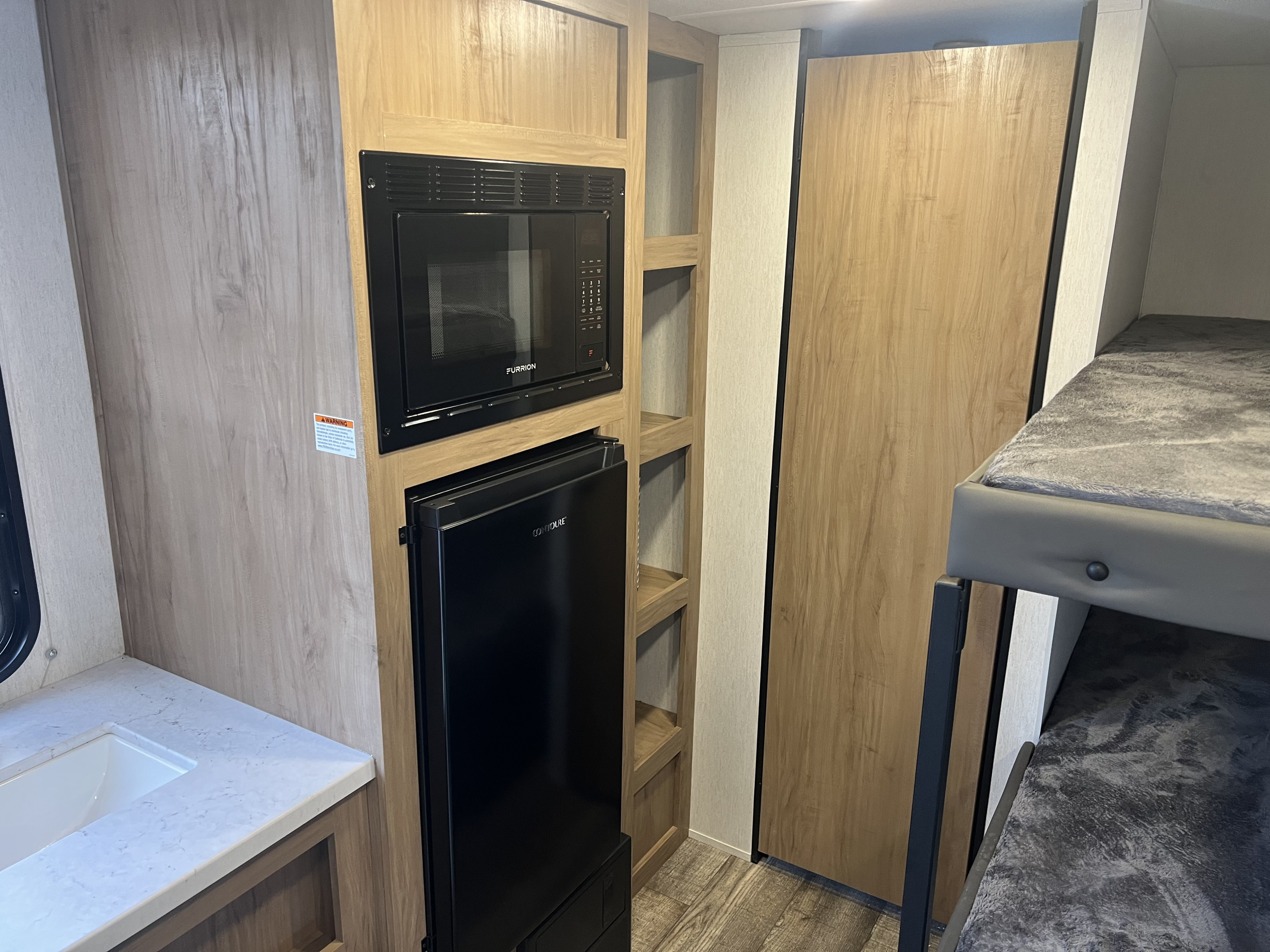 RV rental interior features a compact kitchen with built-in microwave, fridge, sink, and cozy bunk beds.. Forest River Wolf Den 2024