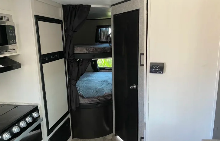 RV rental interior: compact kitchen with stove, microwave, refrigerator, and cozy bunk beds with privacy curtains.. Jayco Jay Flight SLX Rocky Mountain Edition 2022
