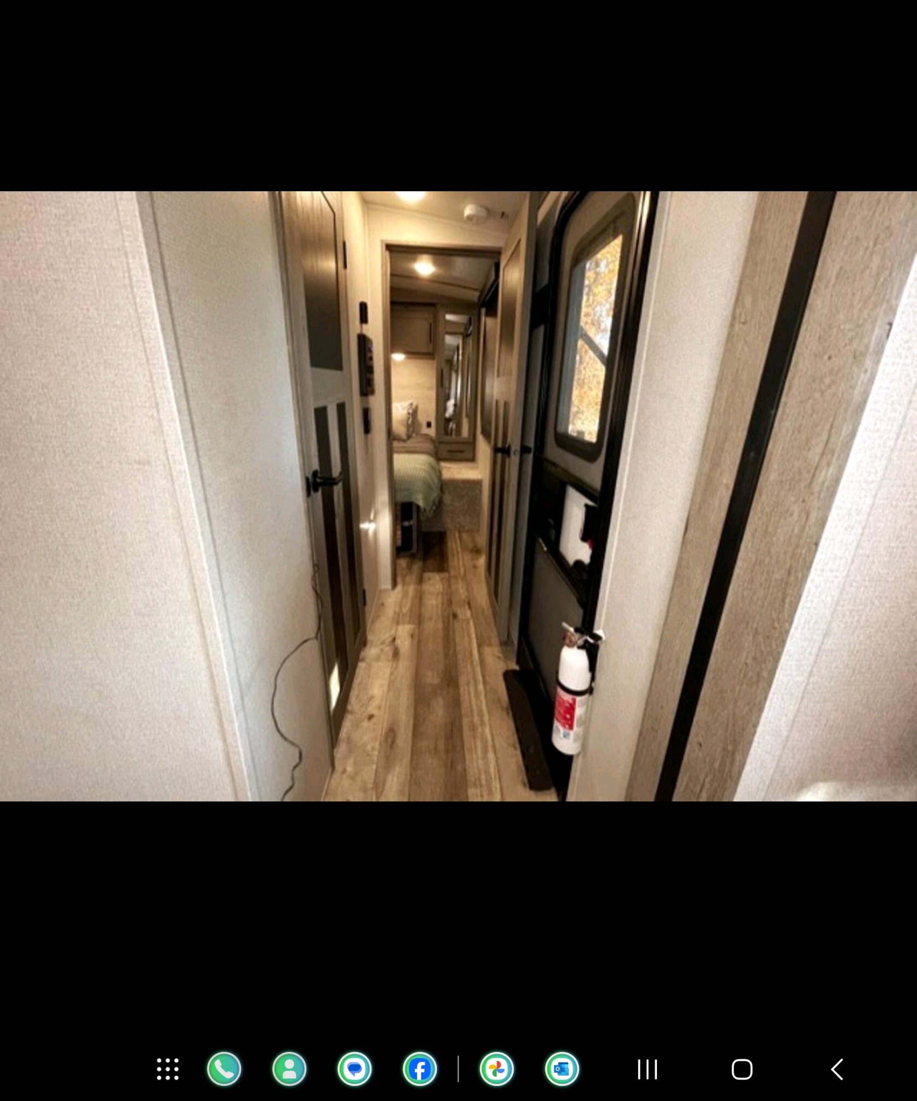 Inside an RV rental: a narrow hallway with wood flooring leads to a bedroom. Fire extinguisher visible by the main door.. Keystone Outback 2022