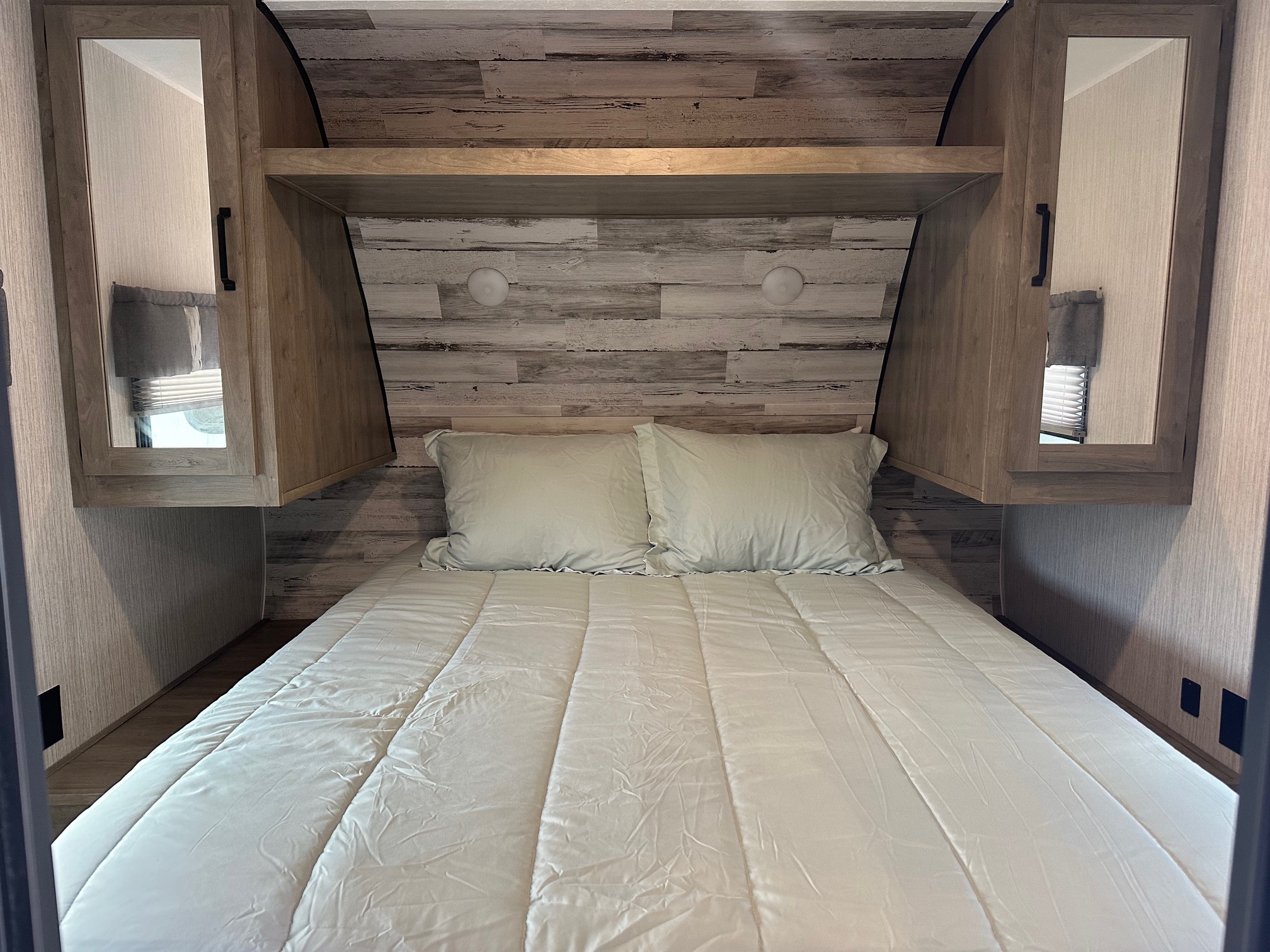 Bright RV rental bedroom with a comfy bed, mirrored storage cabinets, and rustic wood-plank headboard.. Forest River Palomino Puma XLE 2022