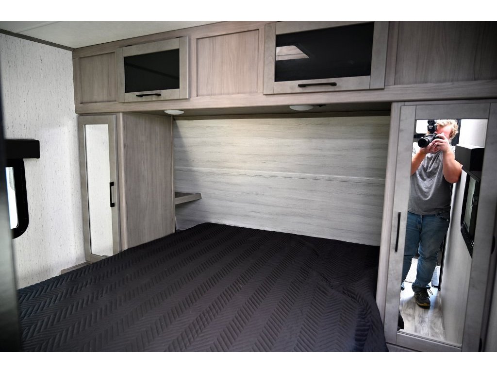 RV rental bedroom with sleek overhead storage, dark bedding, and a mirrored wardrobe for compact comfort.. Dutchmen Kodiak 2022