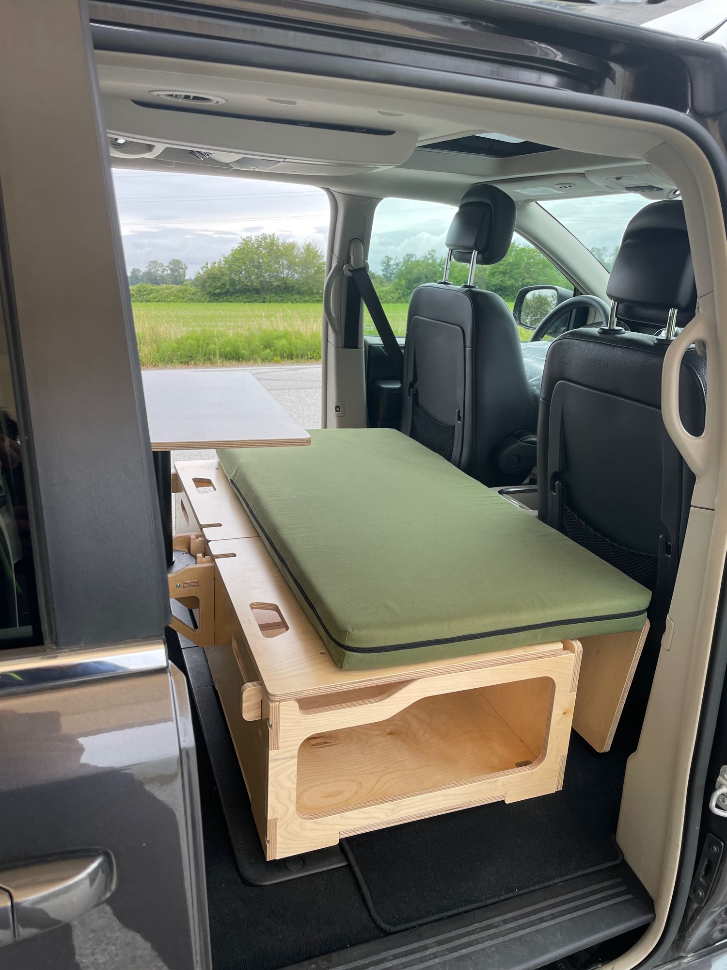 A cozy minivan RV rental conversion provides a green cushioned bed, pull-out table, & storage for road trip adventures.. Dodge Grand Caravan 2015
