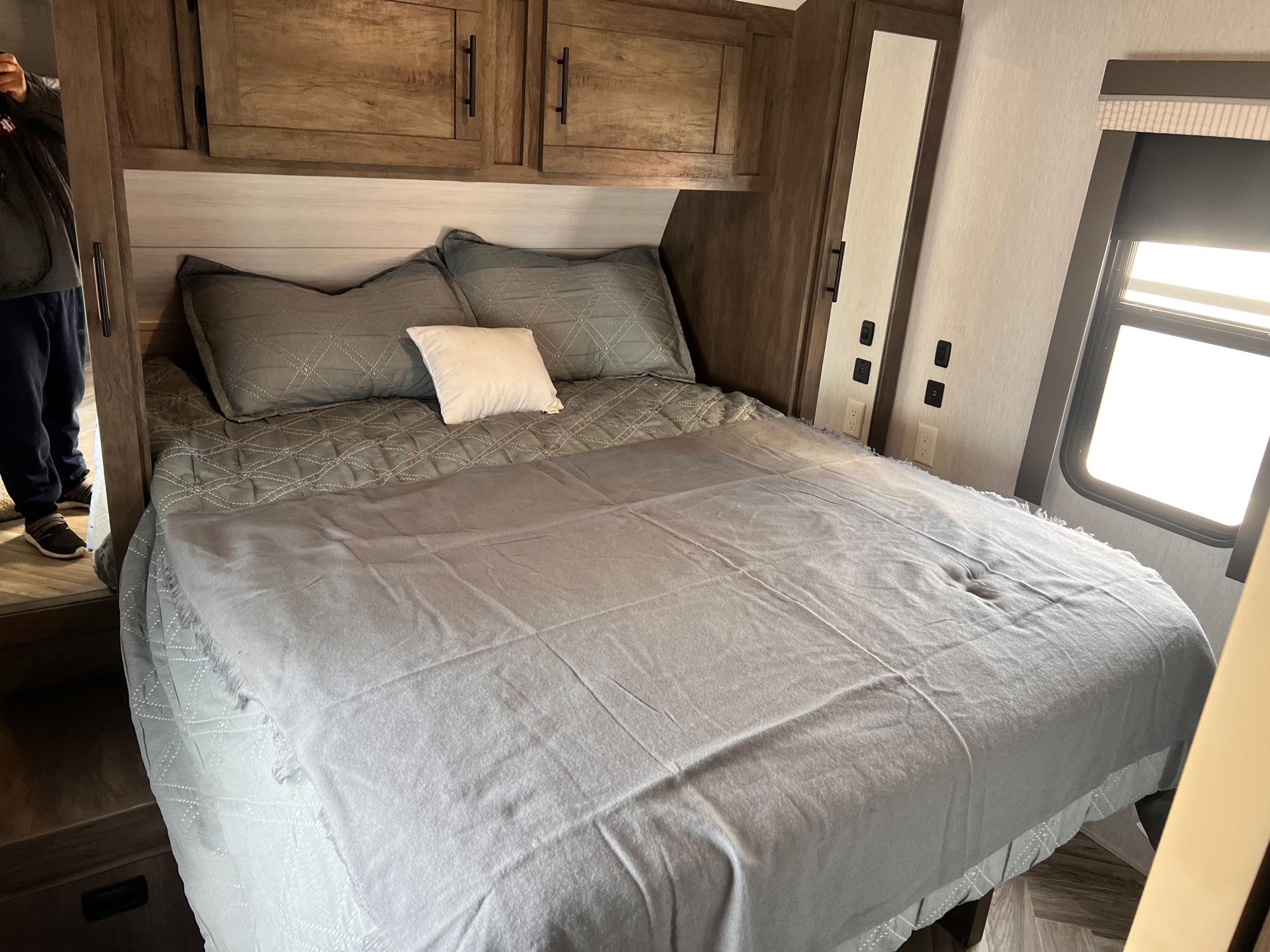 Comfortable RV rental bedroom with neatly made grey bed, overhead cabinets, and a window.. Forest River Salem 2022