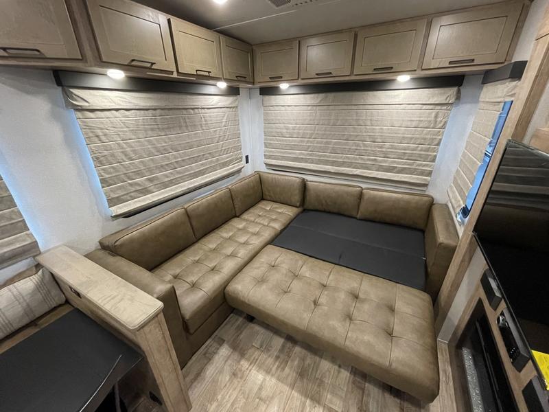 Spacious RV rental interior featuring a tan sectional sofa that converts into a bed, with ample overhead storage.. Keystone Arcadia 2022