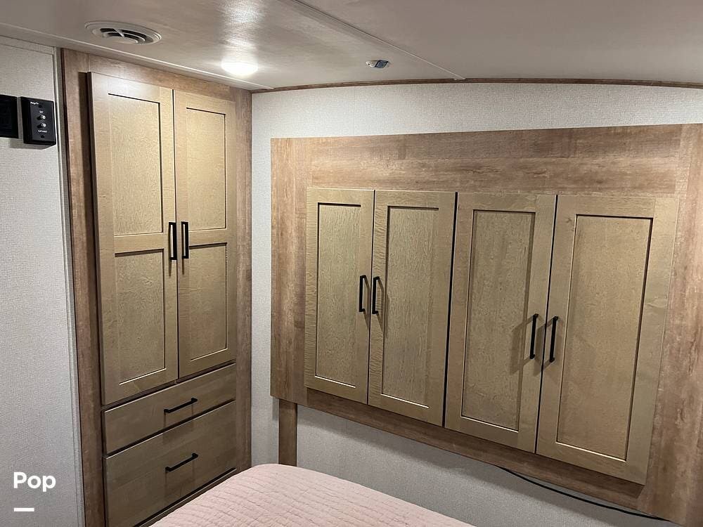 This RV rental bedroom features a wooden wardrobe with drawers, overhead cabinets, and a bed with a pink comforter.. Keystone Arcadia 2022
