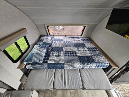 Cozy RV rental interior showcasing a patterned bed, convertible seating, and a window with a green view.. R-Pod R-Pod Trailer 2022