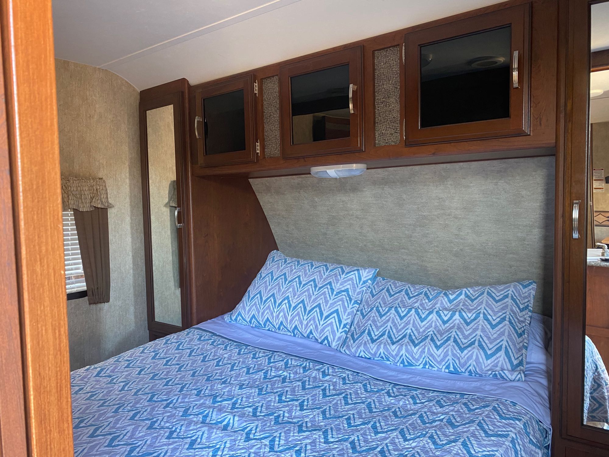 This rv rental bedroom features a bed with blue patterned bedding, wood cabinets, and a mirrored closet. Ready for your next adventure.. Keystone RV Passport Grand Touring 2015