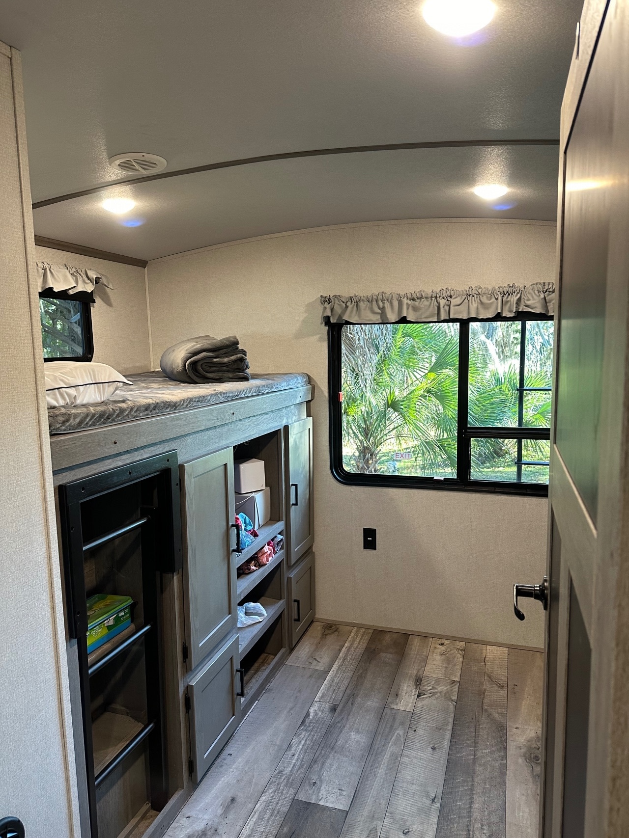 Bright RV rental interior features a cozy bunk bed with ample built-in storage below and scenic windows showing green trees.. Keystone Outback 2021