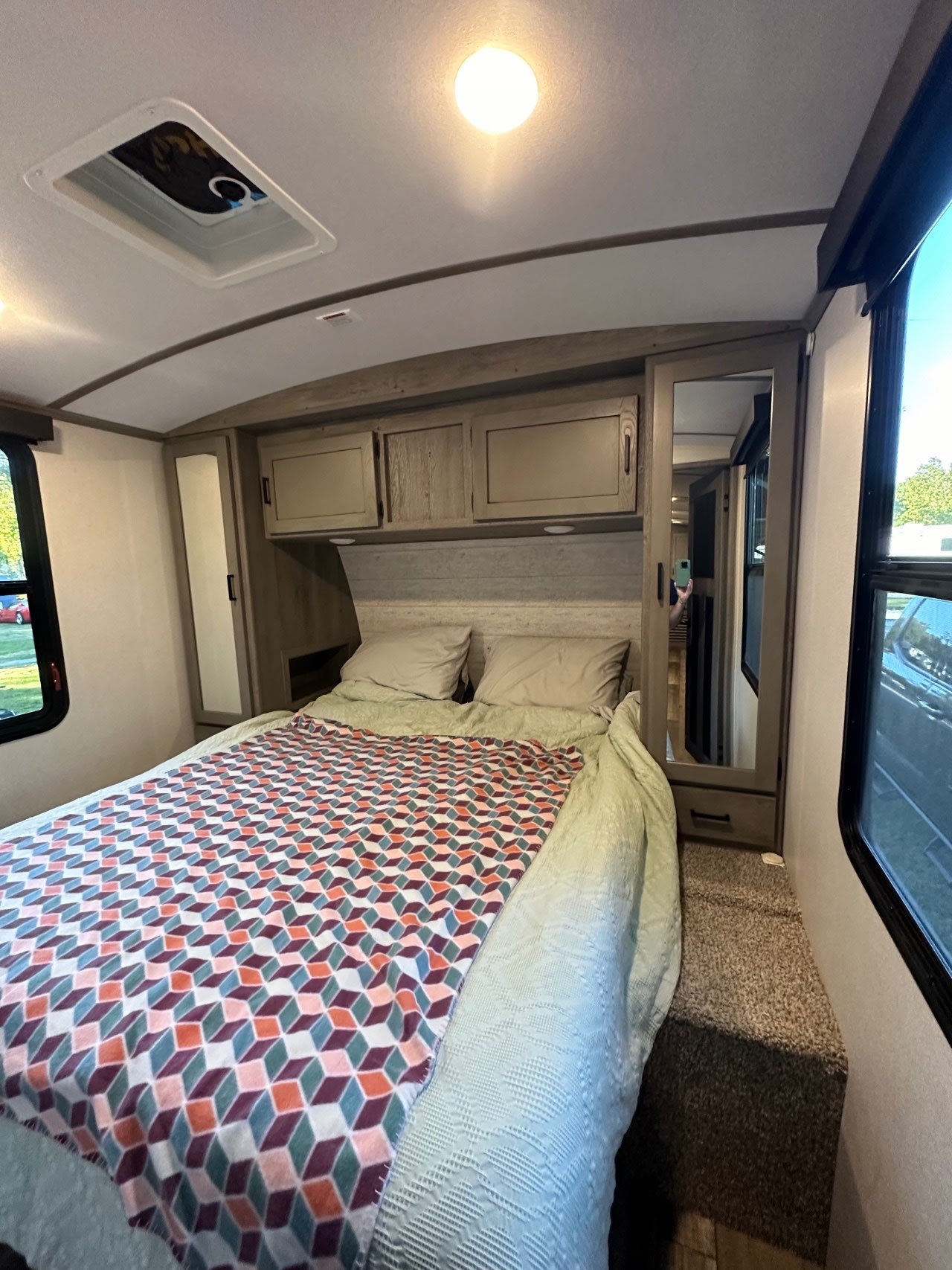 This RV rental bedroom features a comfy bed with a colorful geometric blanket, overhead storage, and a full-length mirrored closet.. Keystone Outback 2021