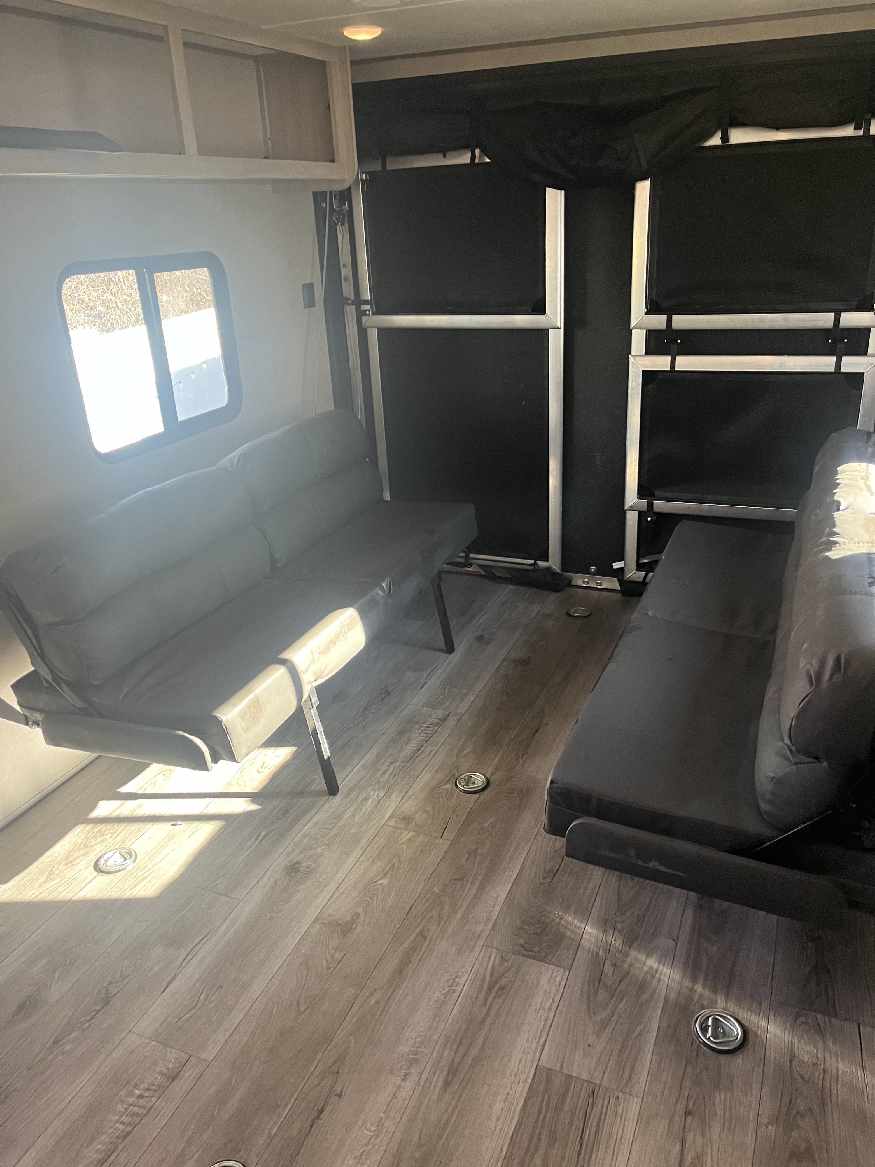 RV rental toy hauler interior featuring dual fold-down sofas/beds, wood-look floor, and cargo tie-downs.. Coachmen Catalina 2022