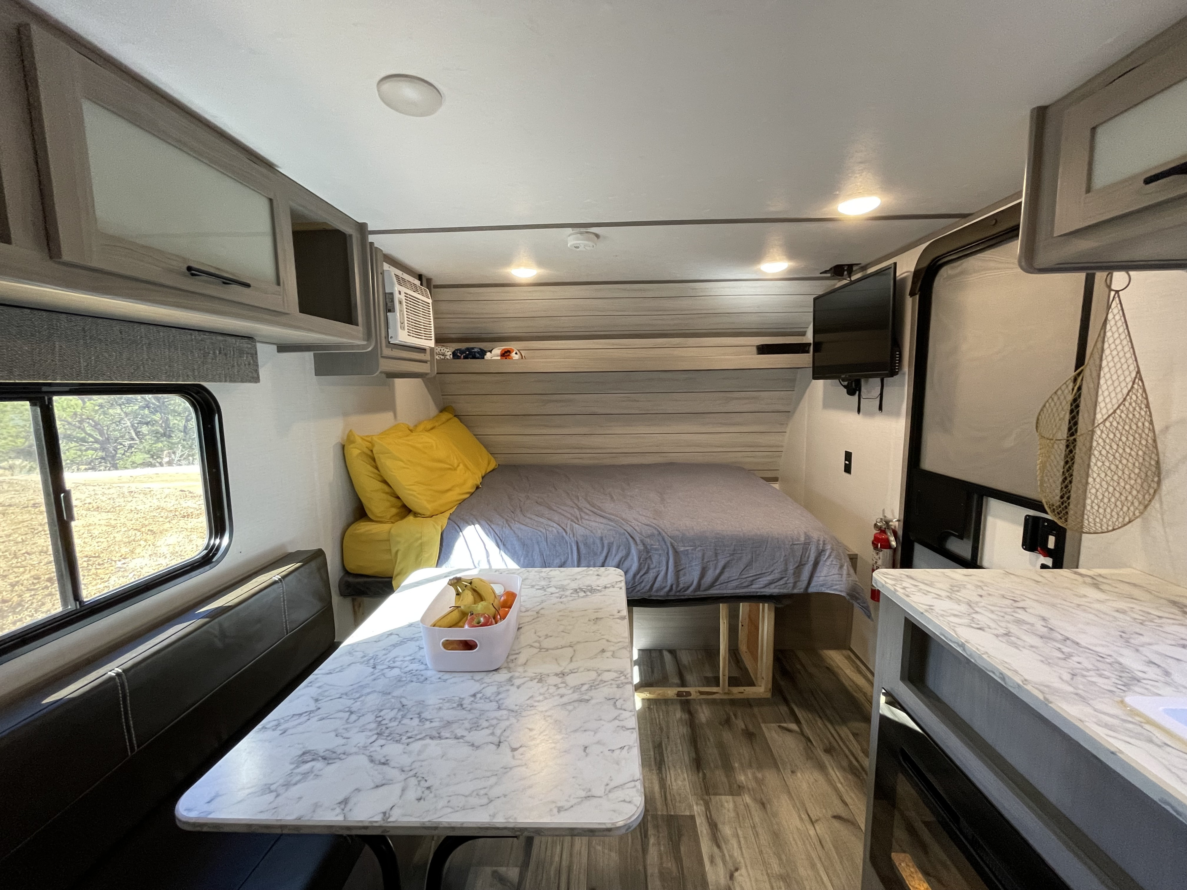 Bright RV rental interior featuring a cozy bed, marble-top dining table, and compact kitchen space for road trips.. Dutchmen Coleman Lantern LT 2023